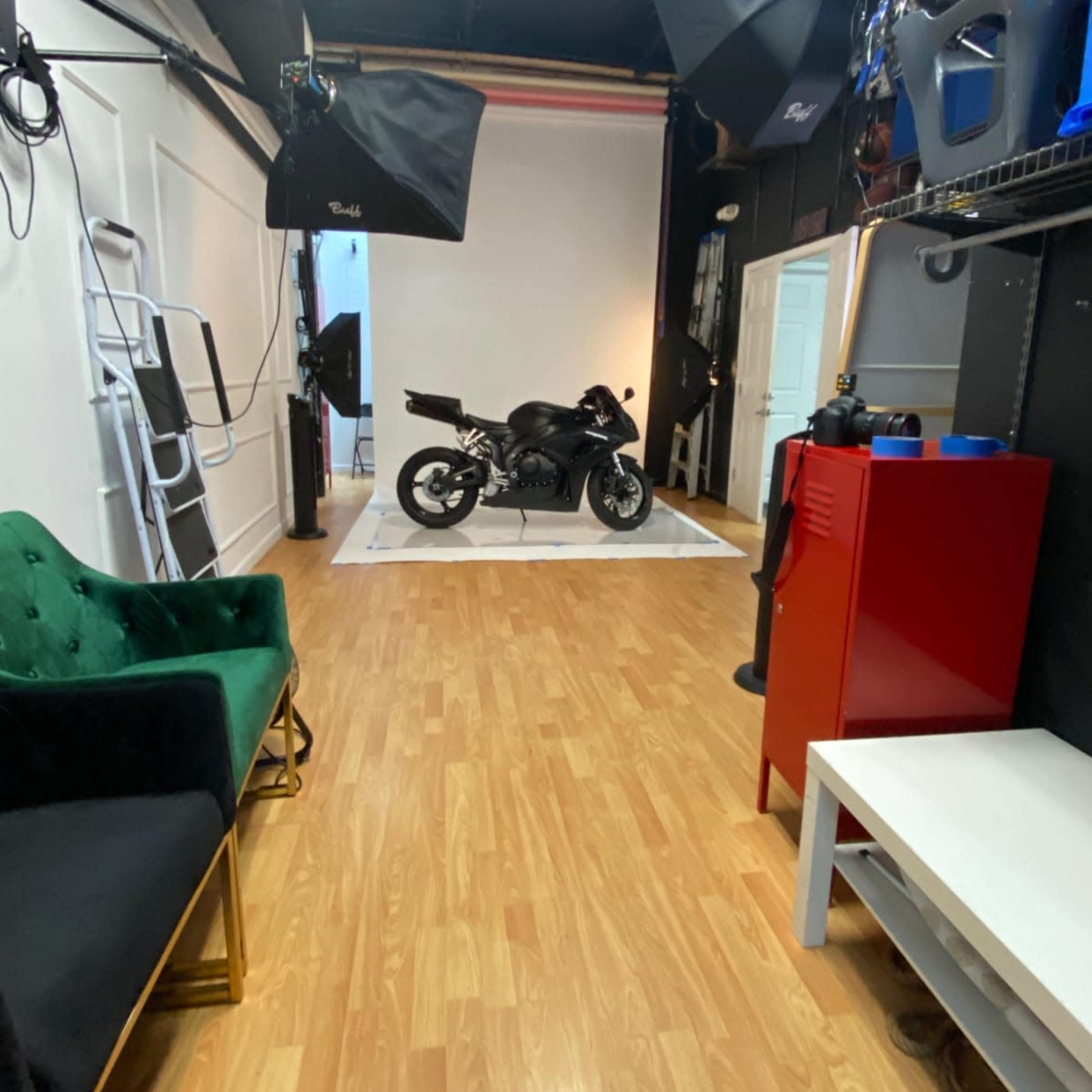 A spacious studio with a motorcycle displayed on a white platform, surrounded by studio lighting and various props.