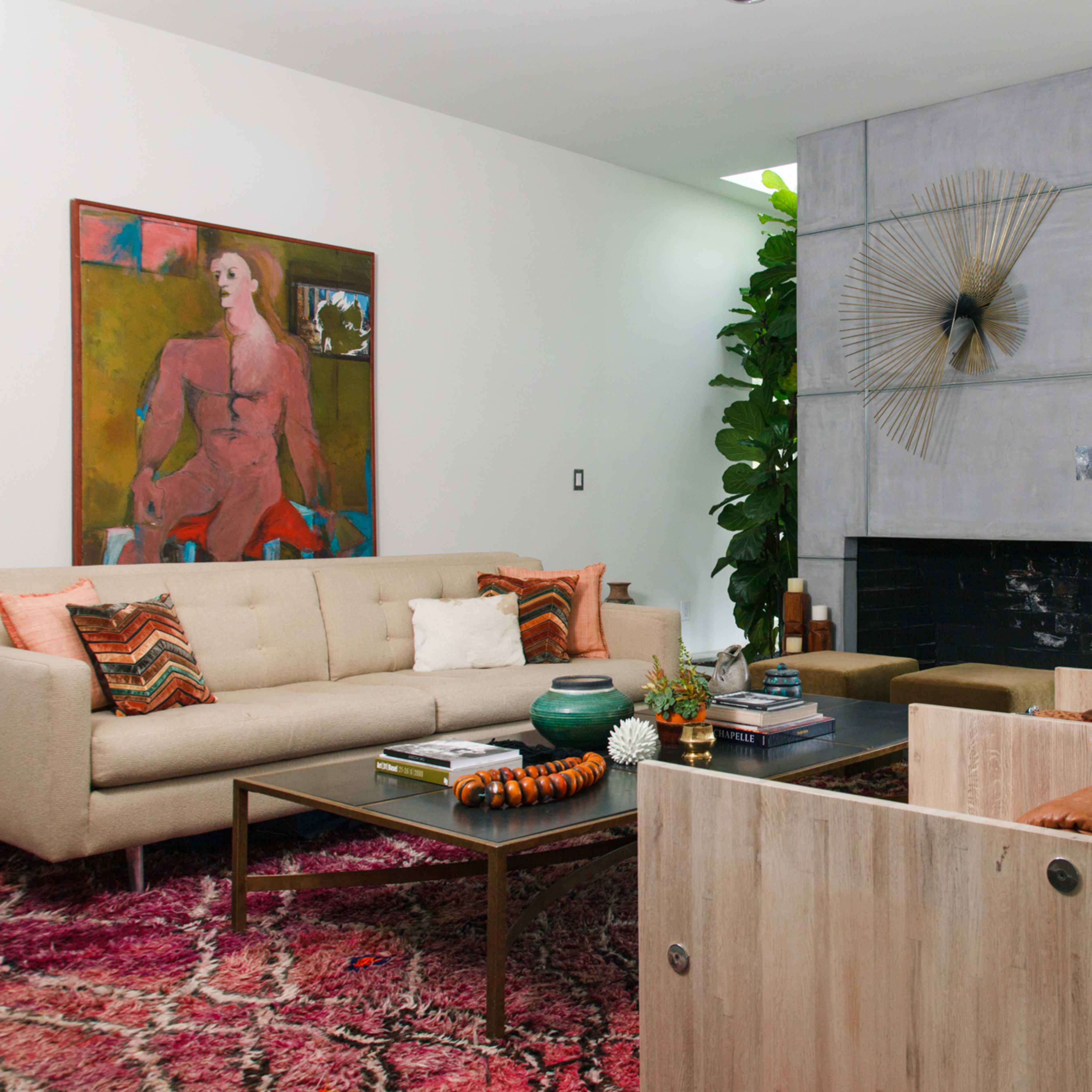 The living room features a light-colored sofa, wooden chairs, a coffee table, and a tall plant, with a painting on the wall and a fireplace.
