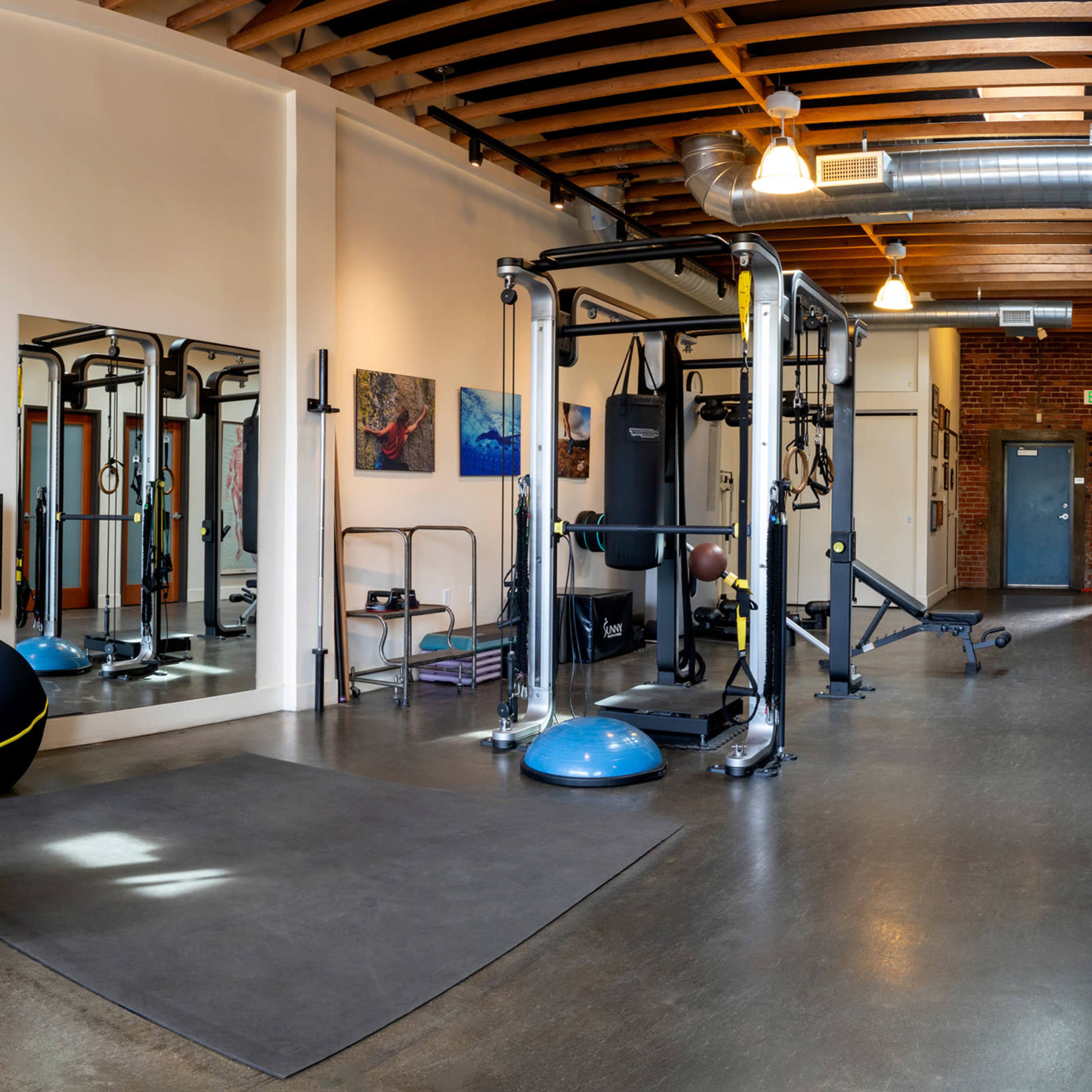 A spacious gym interior featuring various exercise equipment, including weights, stability balls, and yoga mats arranged on the walls.