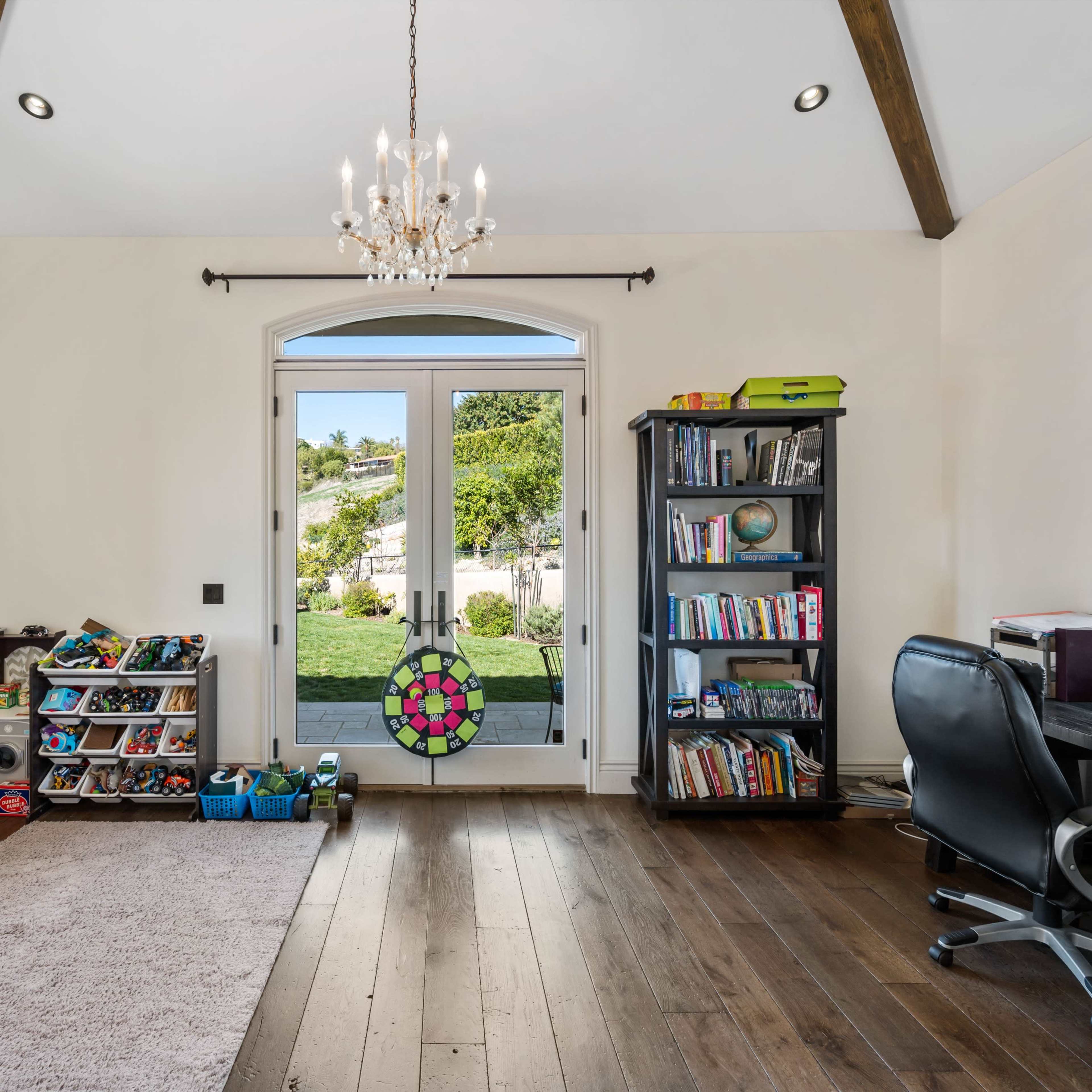 A well-lit room features a door leading to an outdoor area, bookshelves filled with books, and storage for shoes and toys.