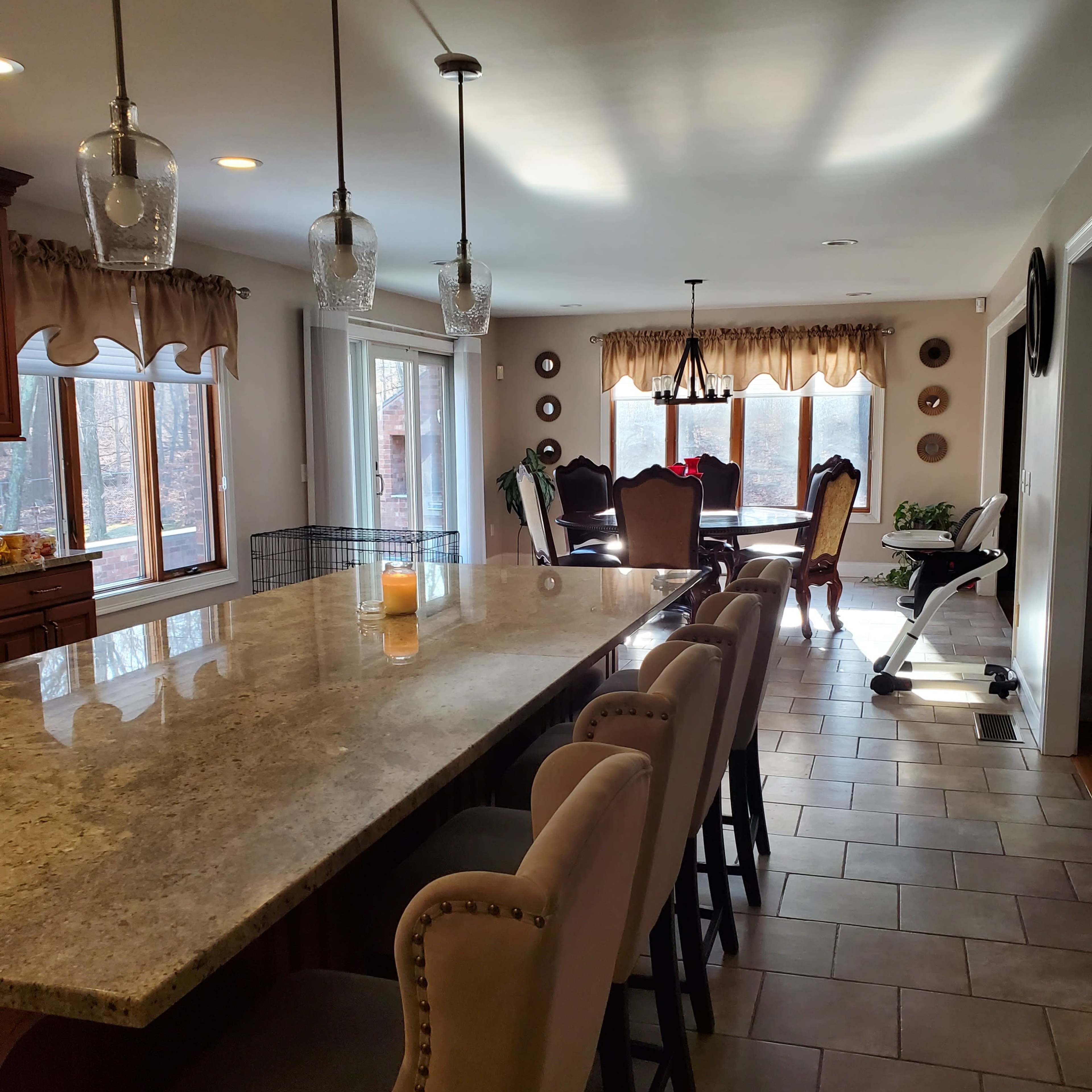 A spacious kitchen with a granite island featuring seating, facing an adjacent dining area with large windows and a polished wooden table.