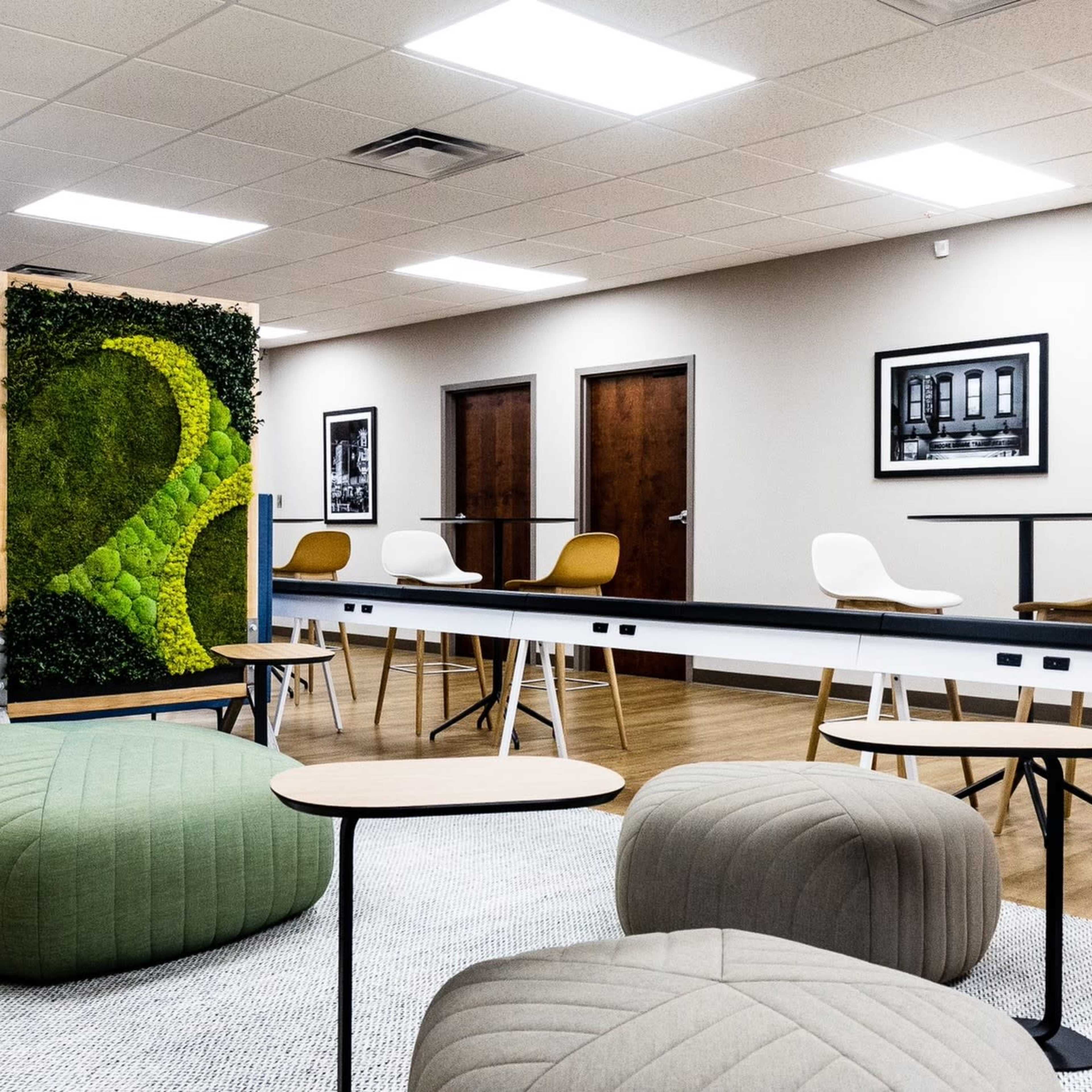 An interior lounge area features a green decorative wall, seating options including poufs and tables, and a mix of white and blue chairs.