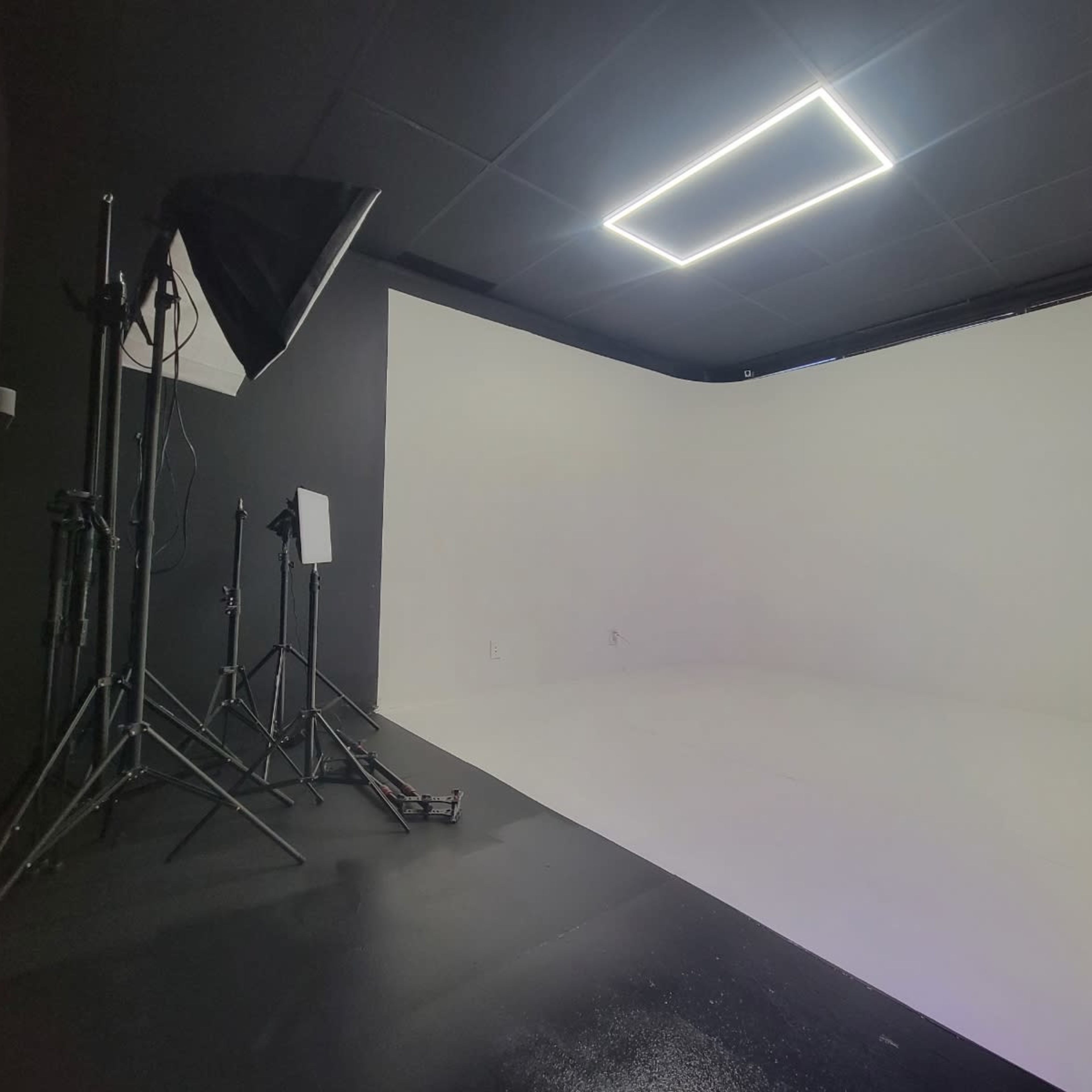 A photography studio with a seamless white backdrop, lighting equipment, and a clean black floor.