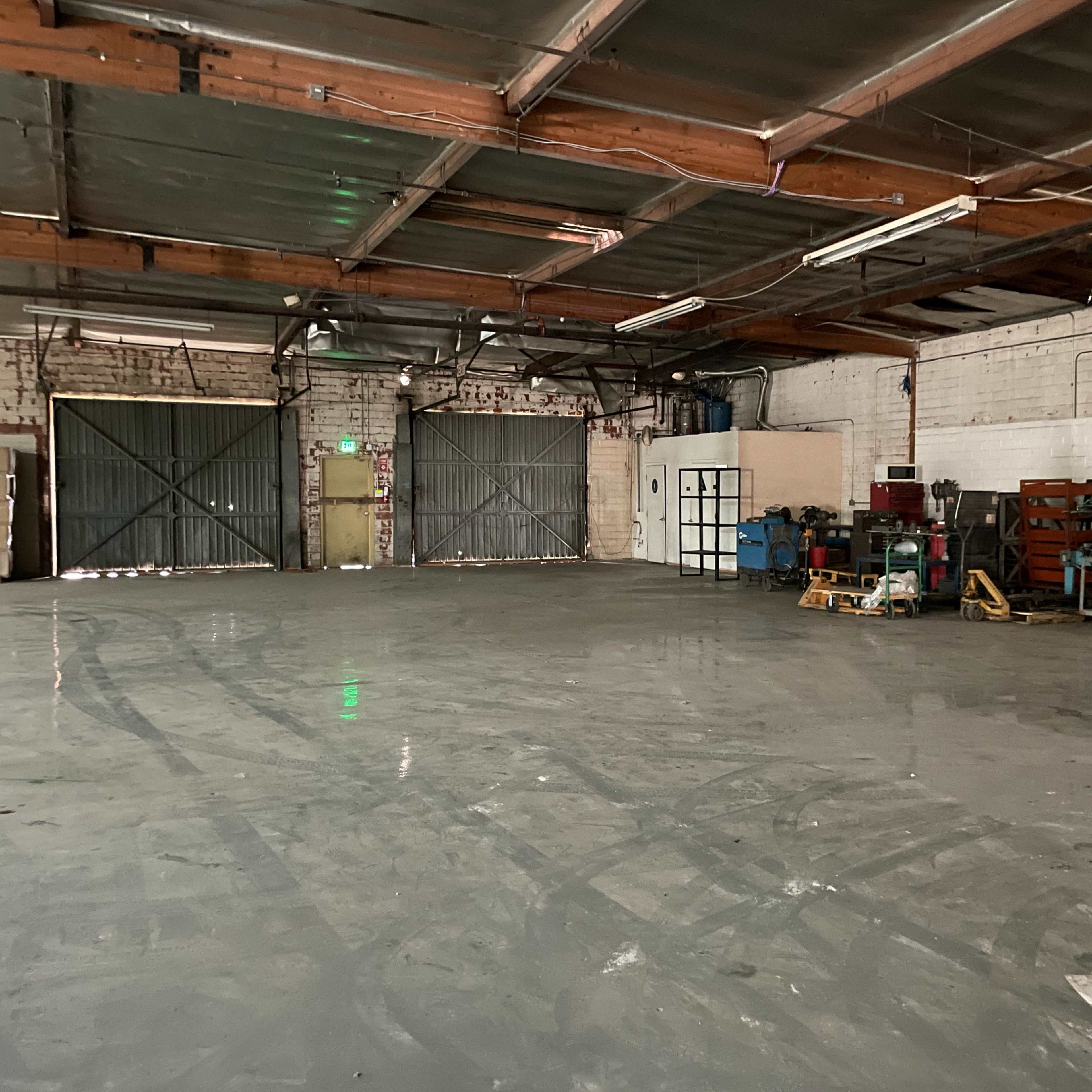 A spacious warehouse interior features concrete flooring, exposed beams, and various industrial equipment along one side.