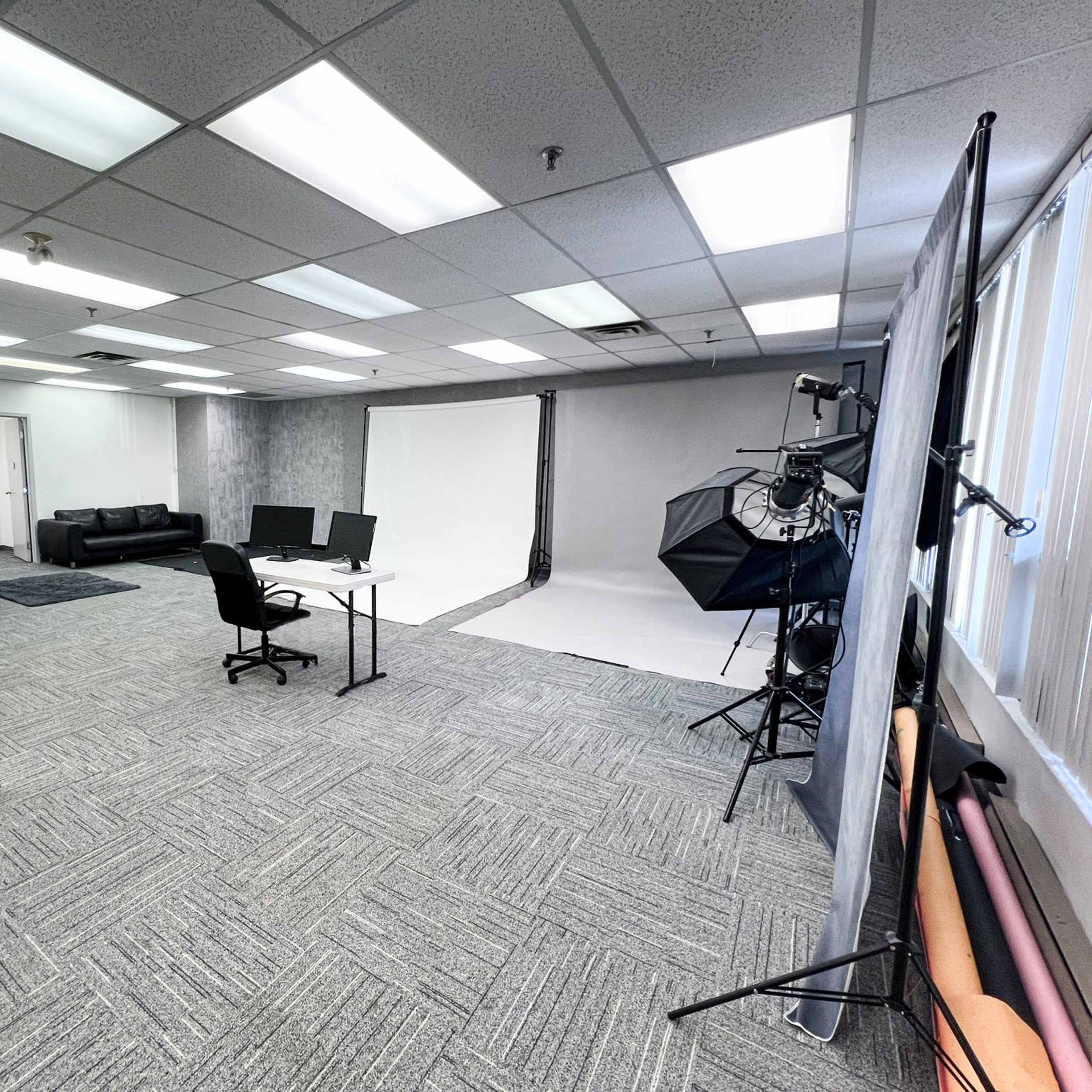 A photography studio with two workstations, a black couch, and equipment for photo shoots, including backdrops and lighting setups.
