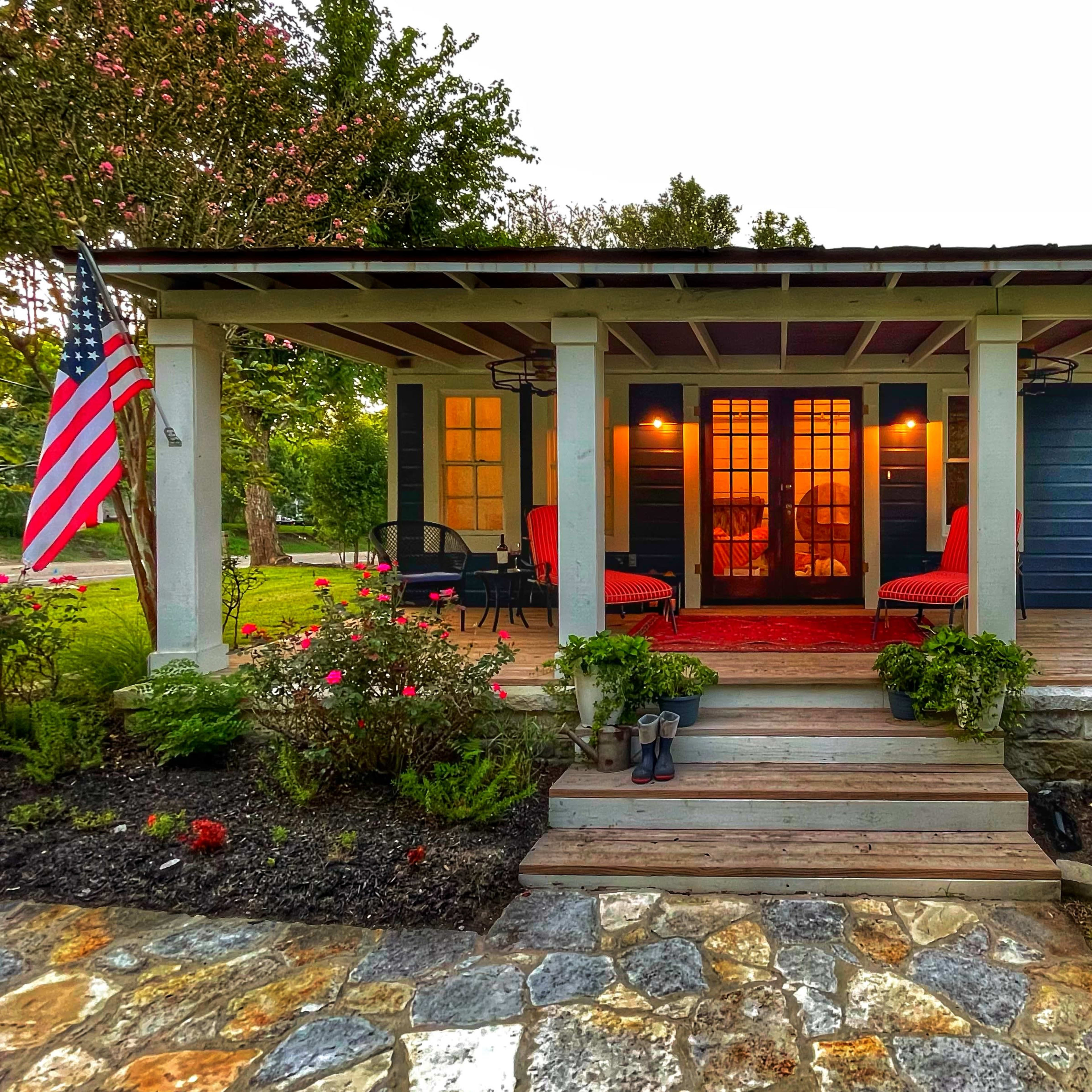 A charming front porch with red seating, surrounded by colorful flowers and a flag, welcomes visitors to a house.