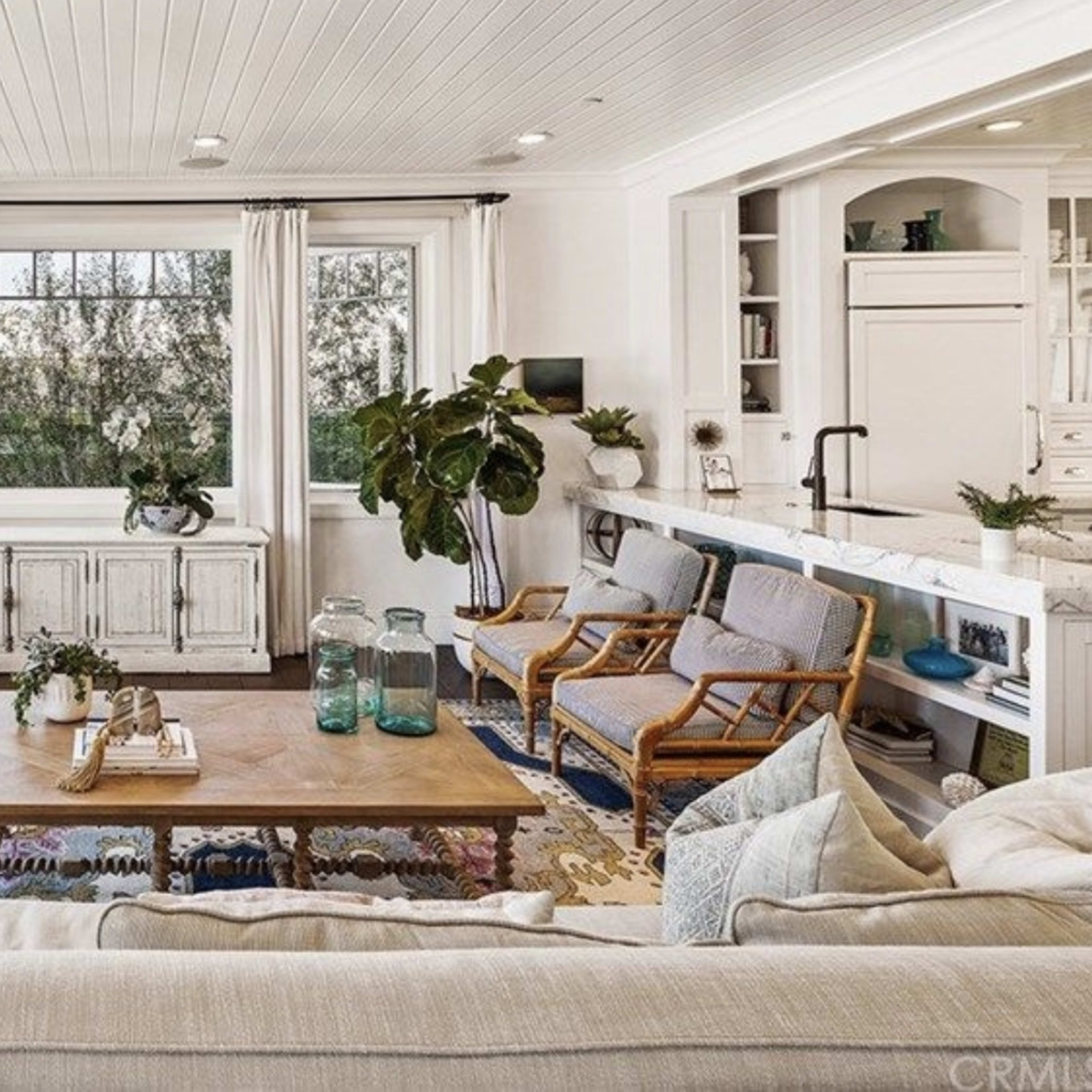 A bright living room features a large window with a view, a wooden coffee table at the center, and comfortable seating arranged around it.