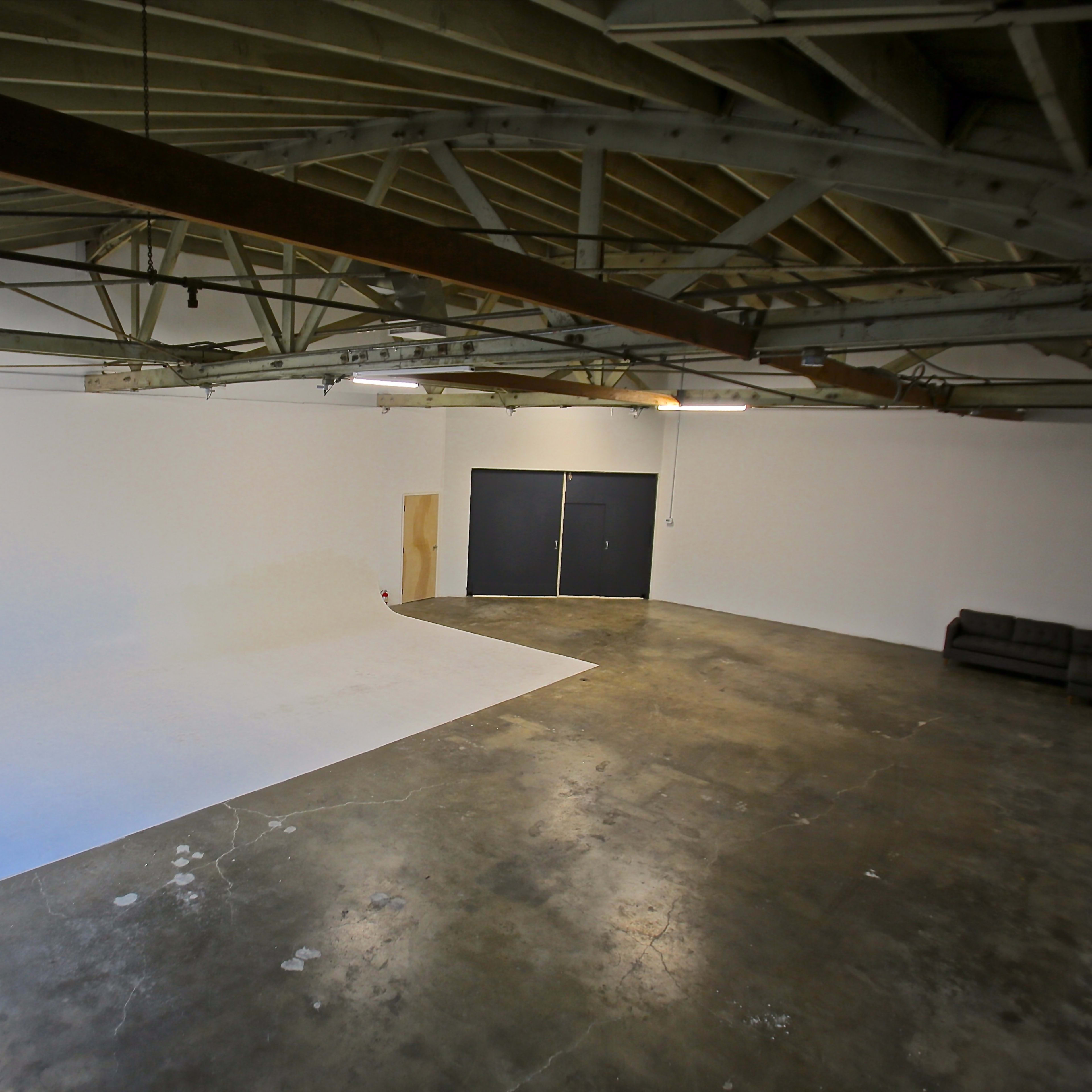 A large, empty studio space with a white backdrop, concrete floor, and a couch against the wall.