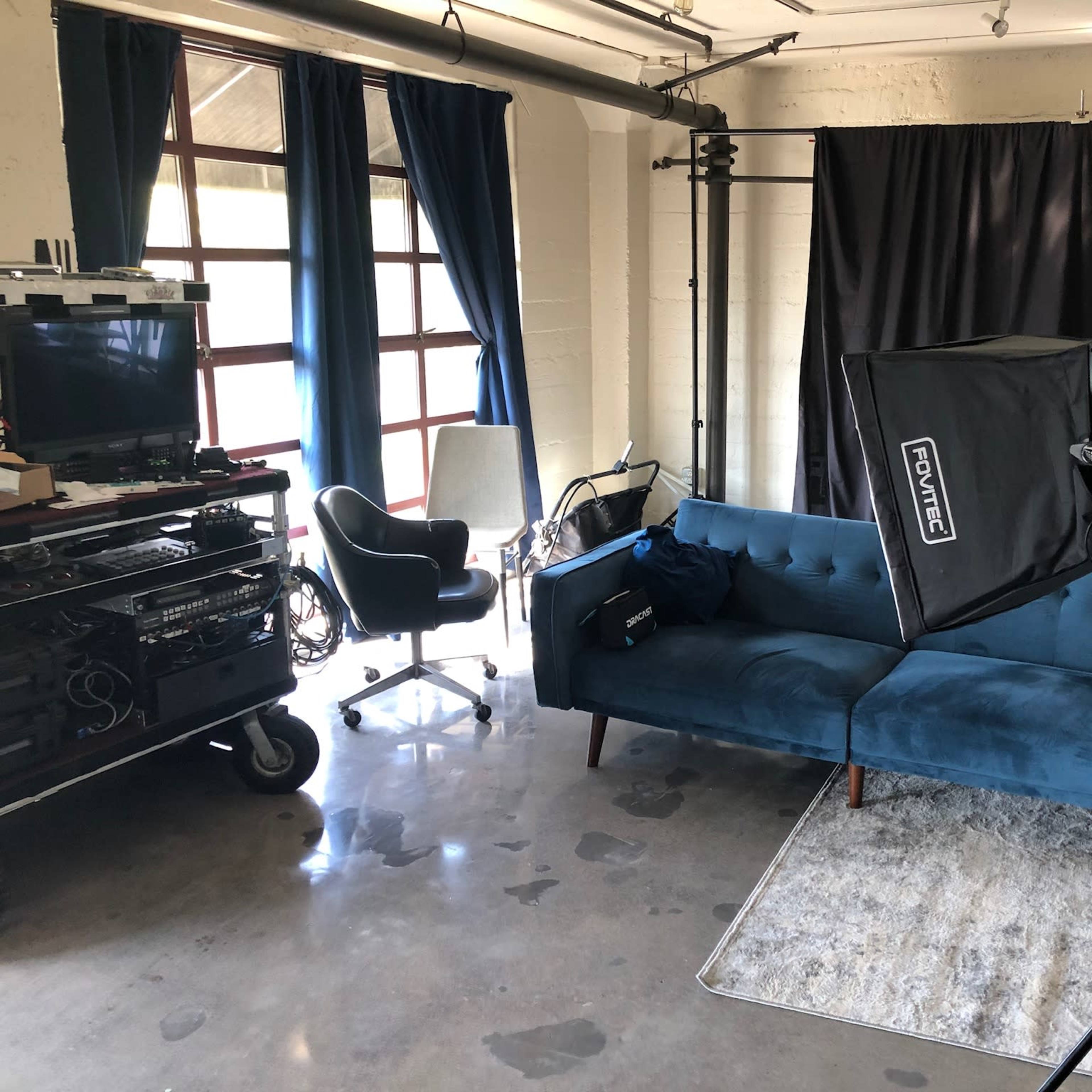 A photography studio with a blue couch, a light setup, and a backdrop on one side, alongside various pieces of equipment.