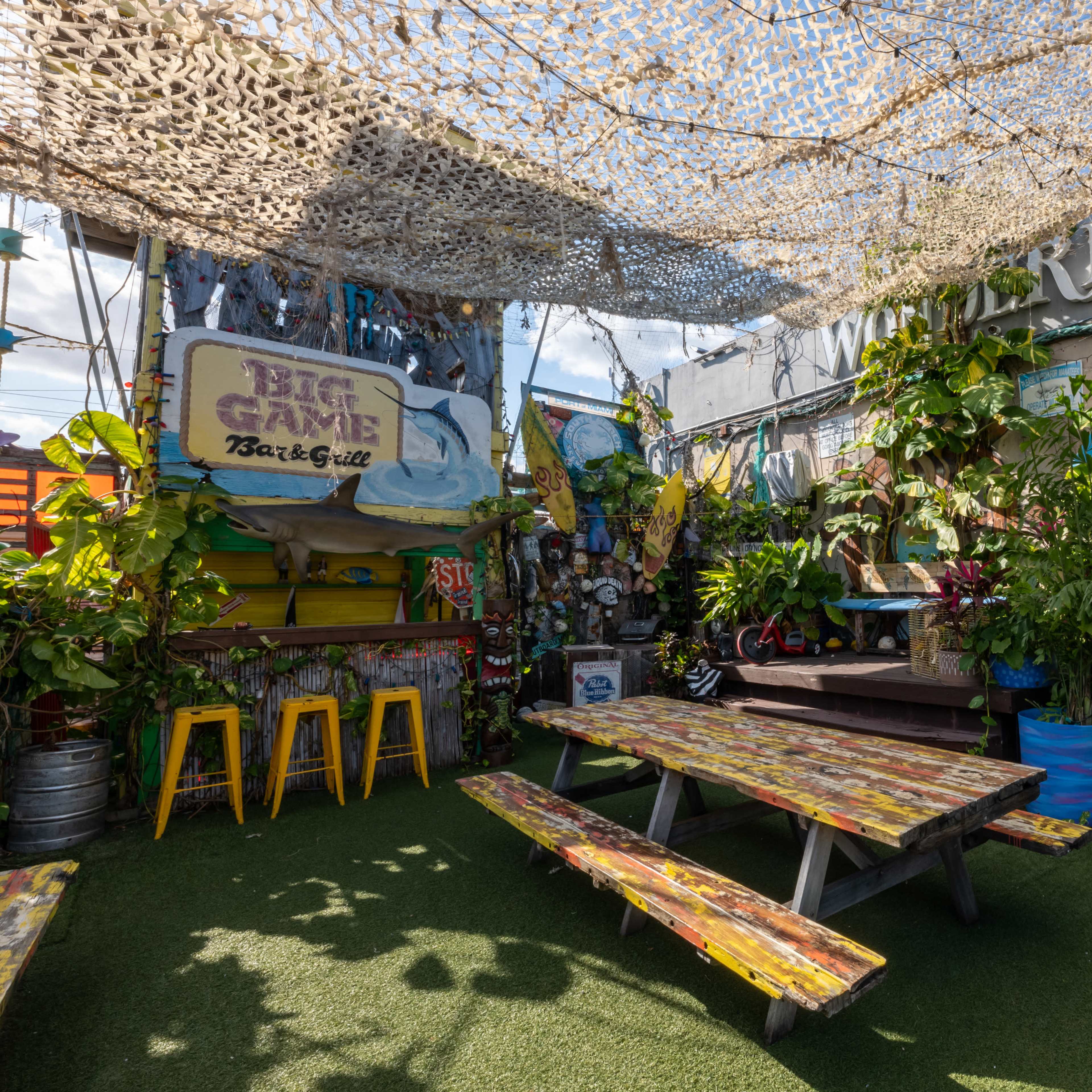 A vibrant outdoor dining area with colorful picnic tables, lush greenery, and a shaded canopy.