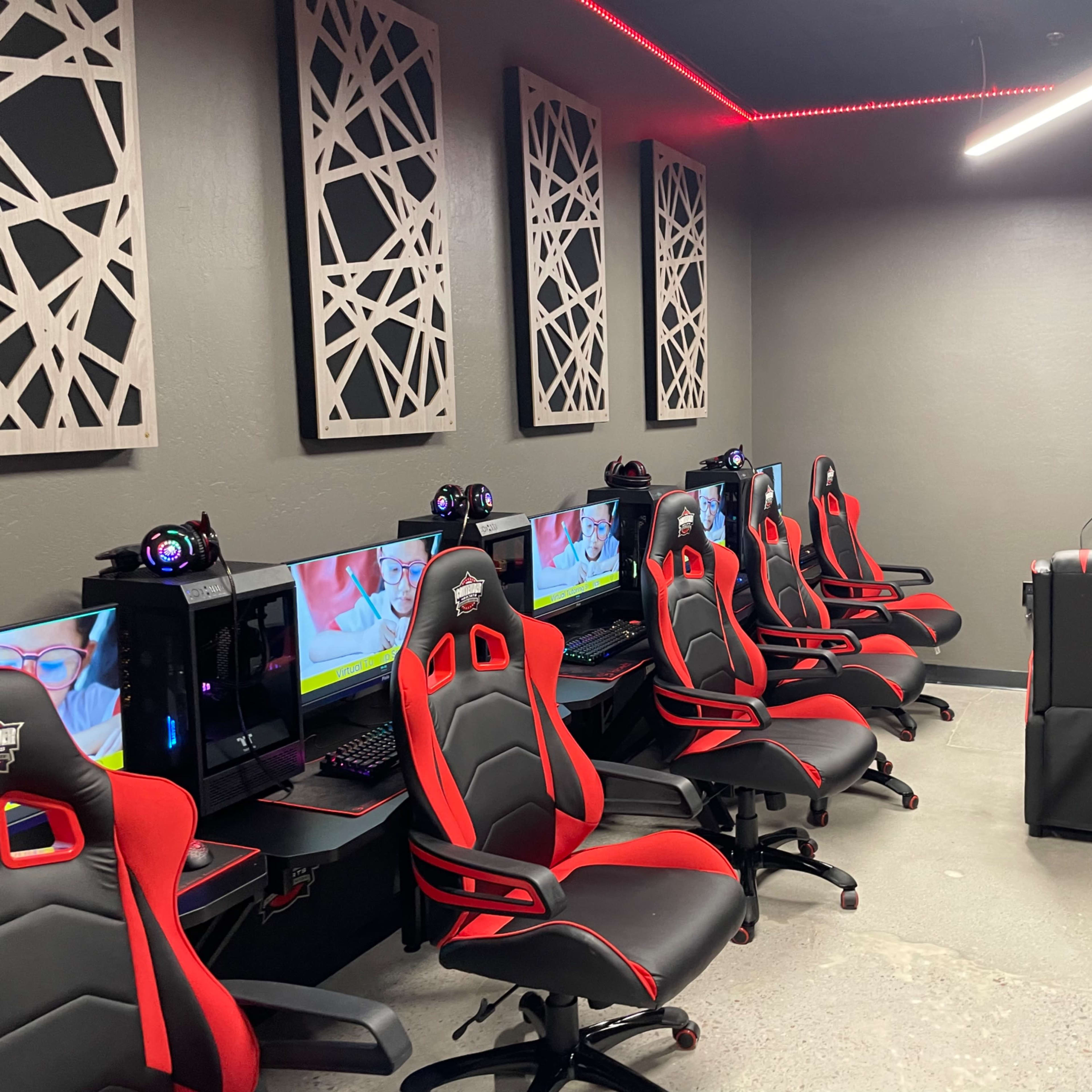 A gaming room equipped with multiple desktop computer setups and ergonomic chairs arranged along the walls.