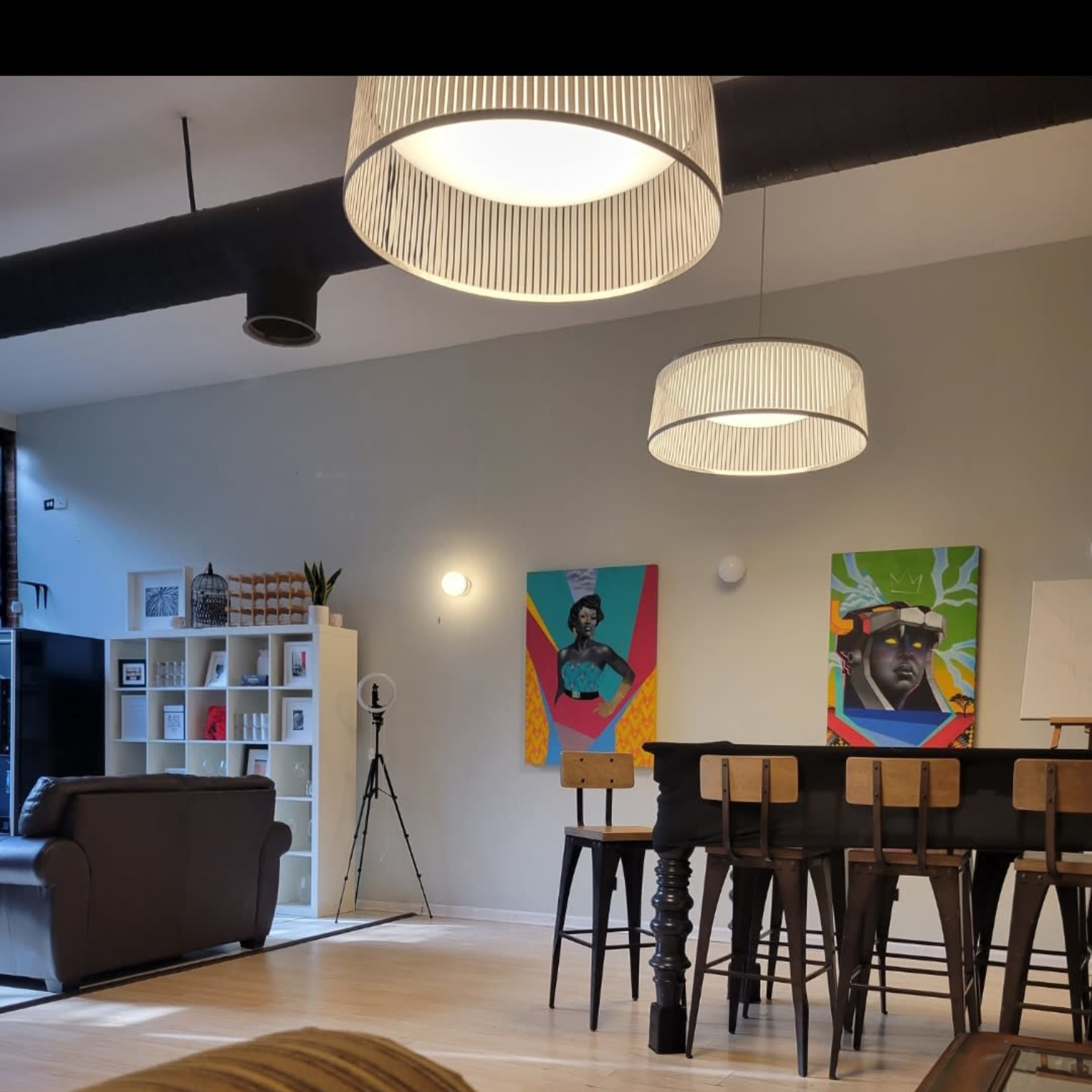 A spacious room with two colorful wall paintings, a large table with stools, and a seating area featuring a couch.