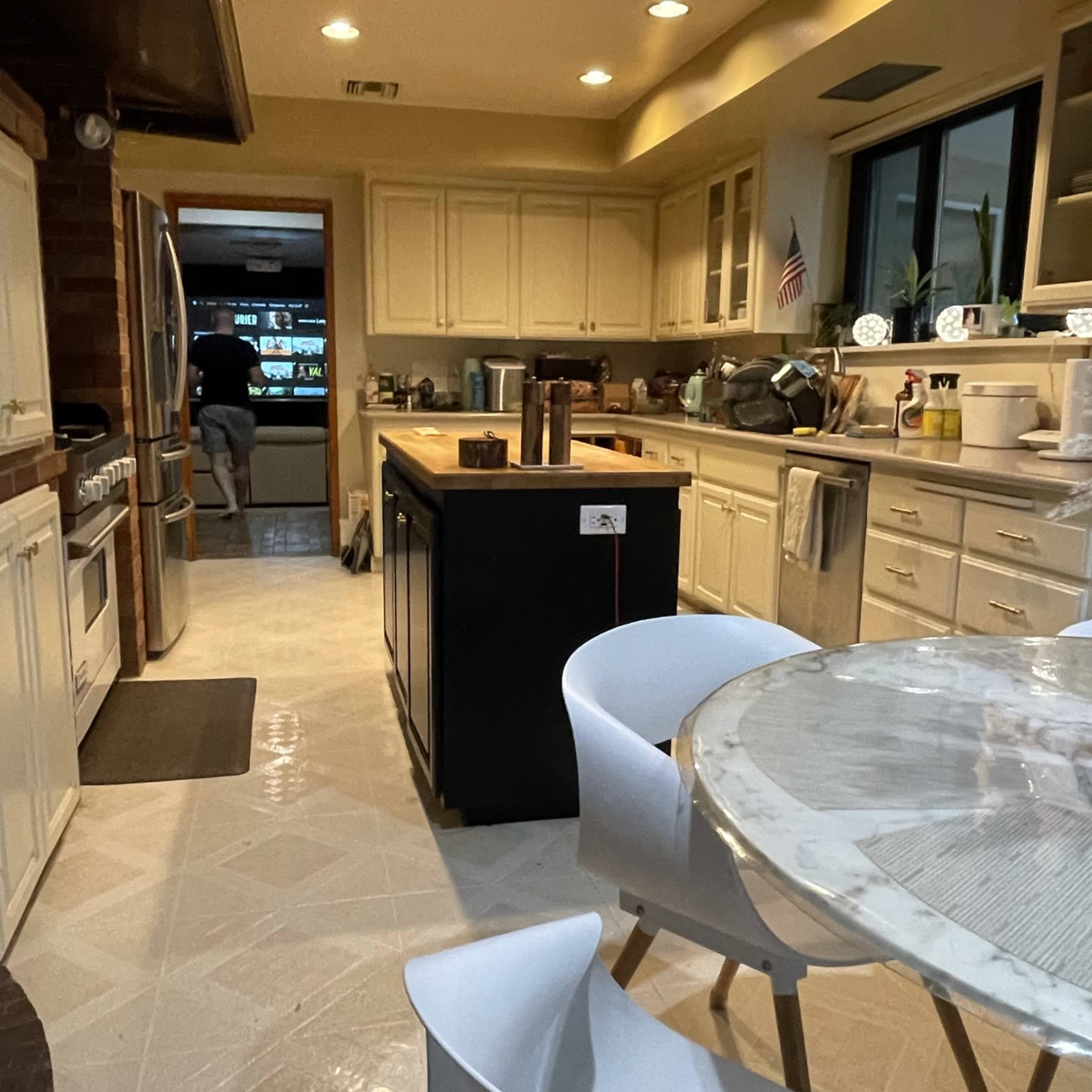 The kitchen features a central island with an adjacent dining area, illuminated by overhead lights, and includes appliances and decor along the countertops.