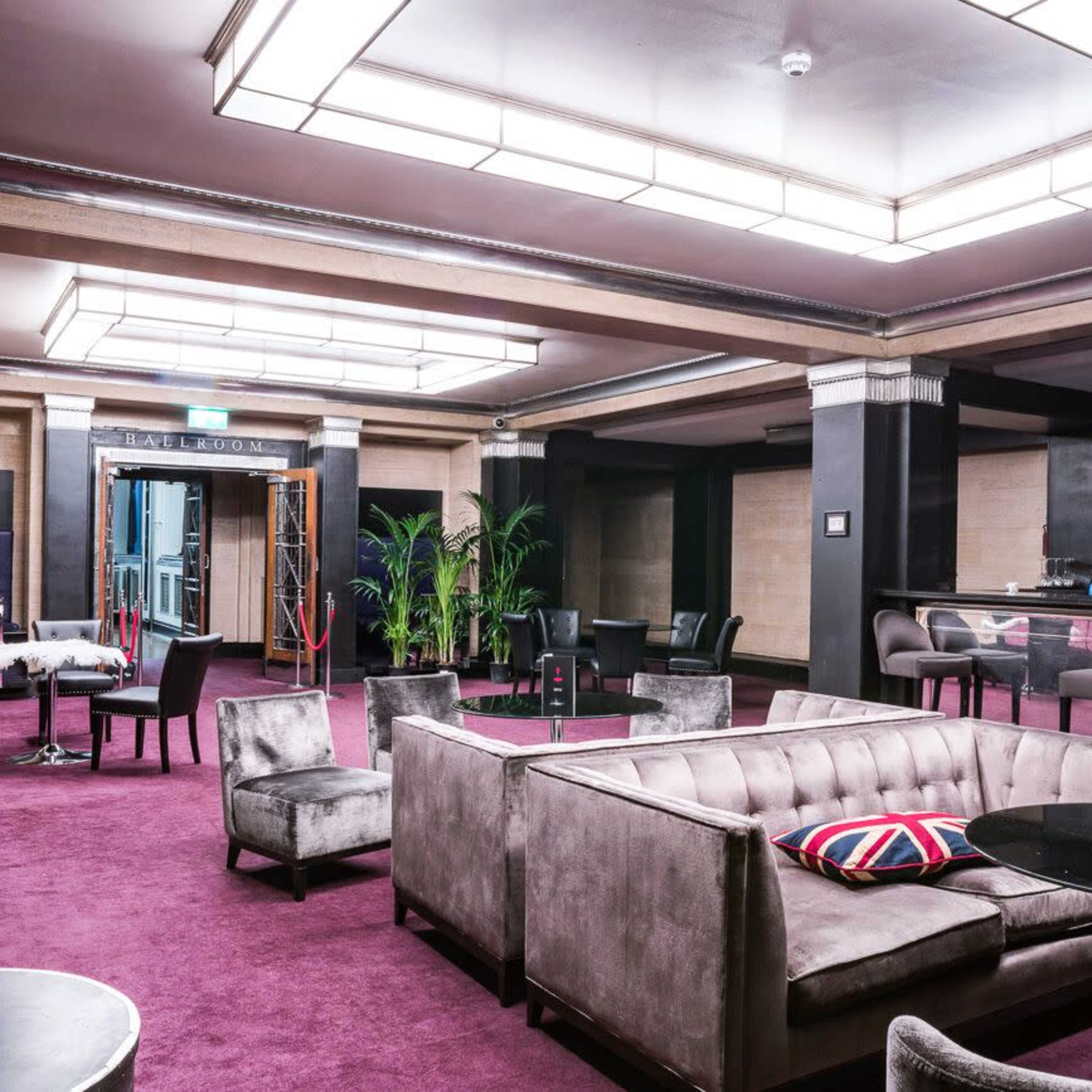 A stylish lounge with plush seating, a bar, and a purple carpet, featuring a mix of modern and vintage decor elements.