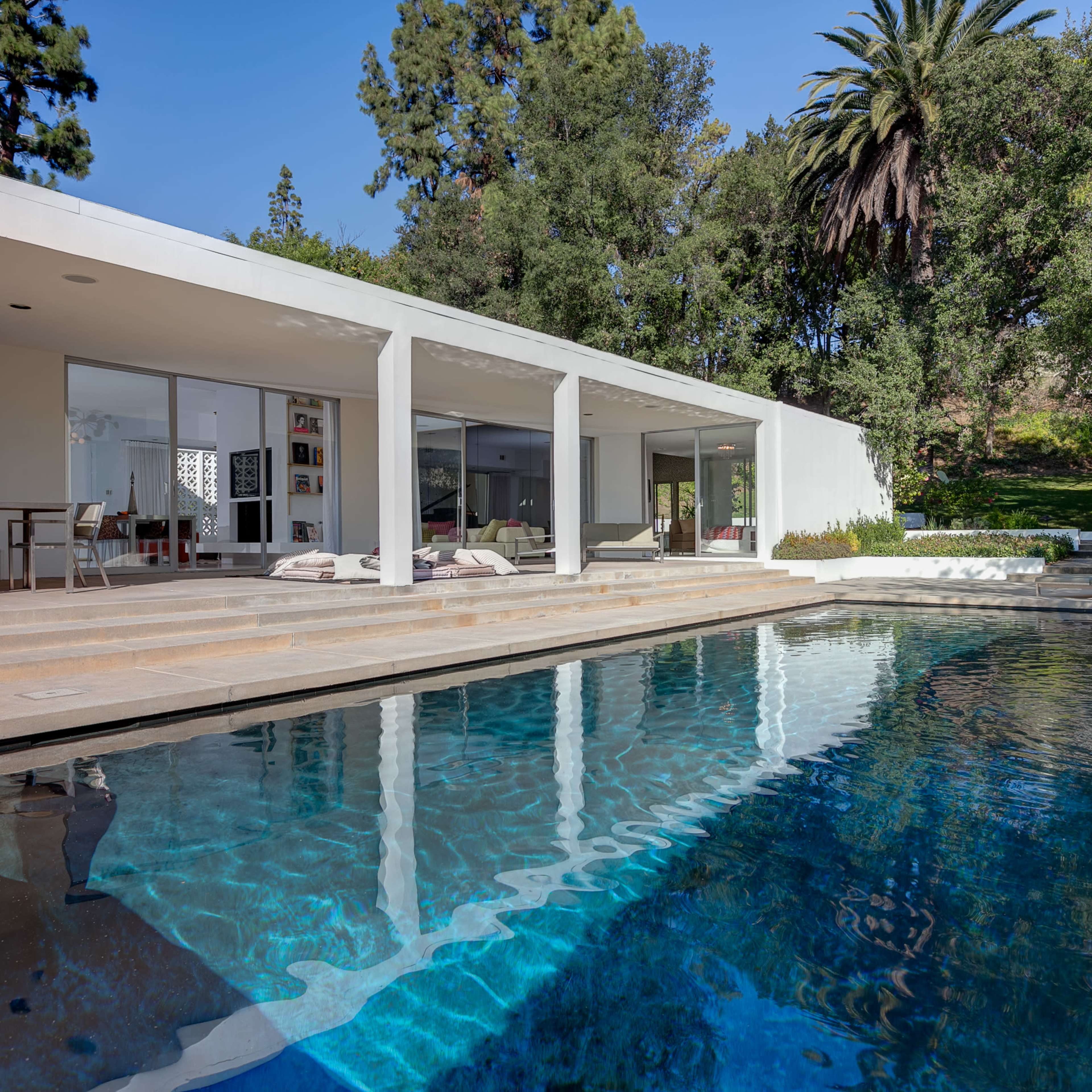 A modern house with large glass windows overlooking a swimming pool surrounded by greenery.