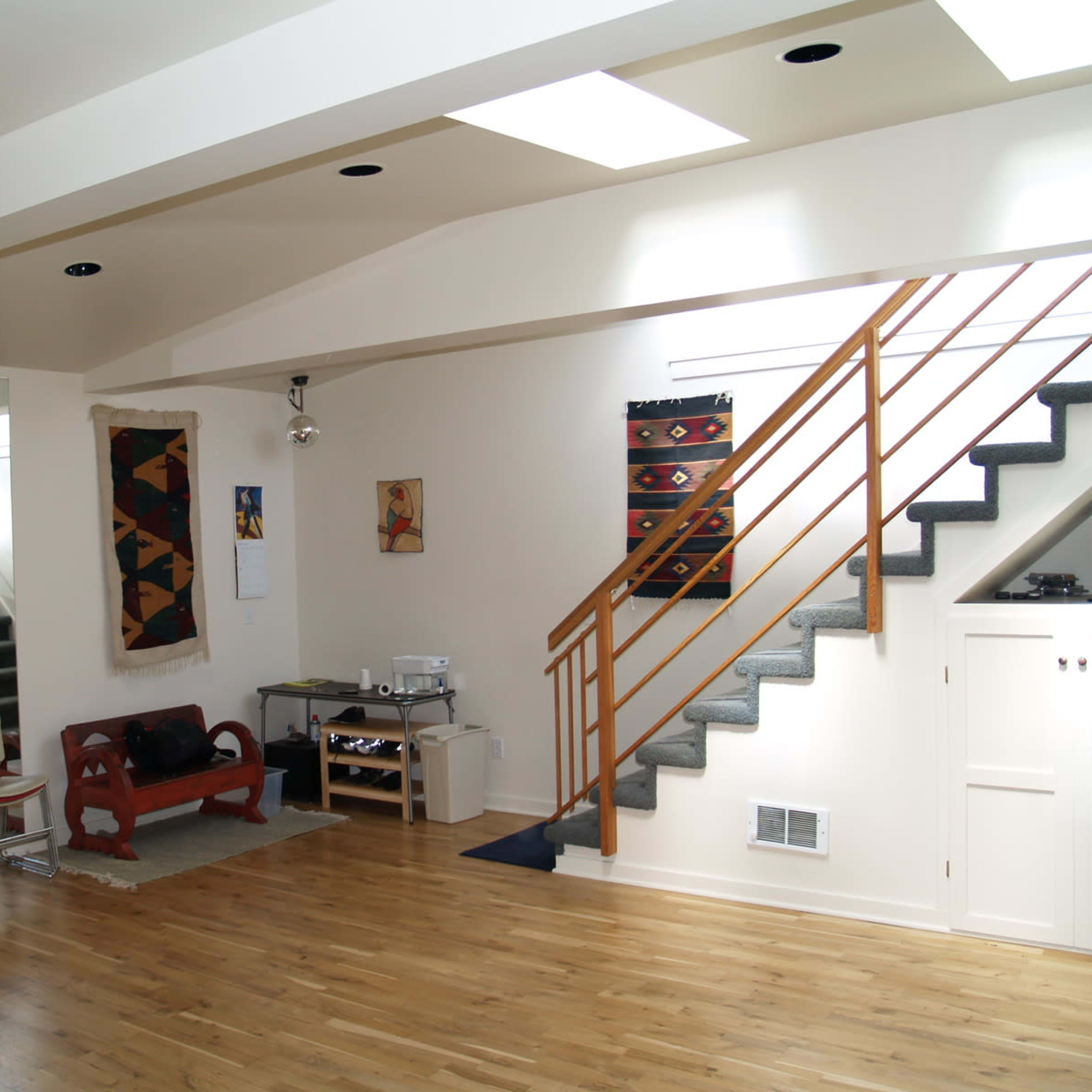 An interior space featuring a wooden floor, a staircase with wooden railings, and a seating area with a chair and small table.