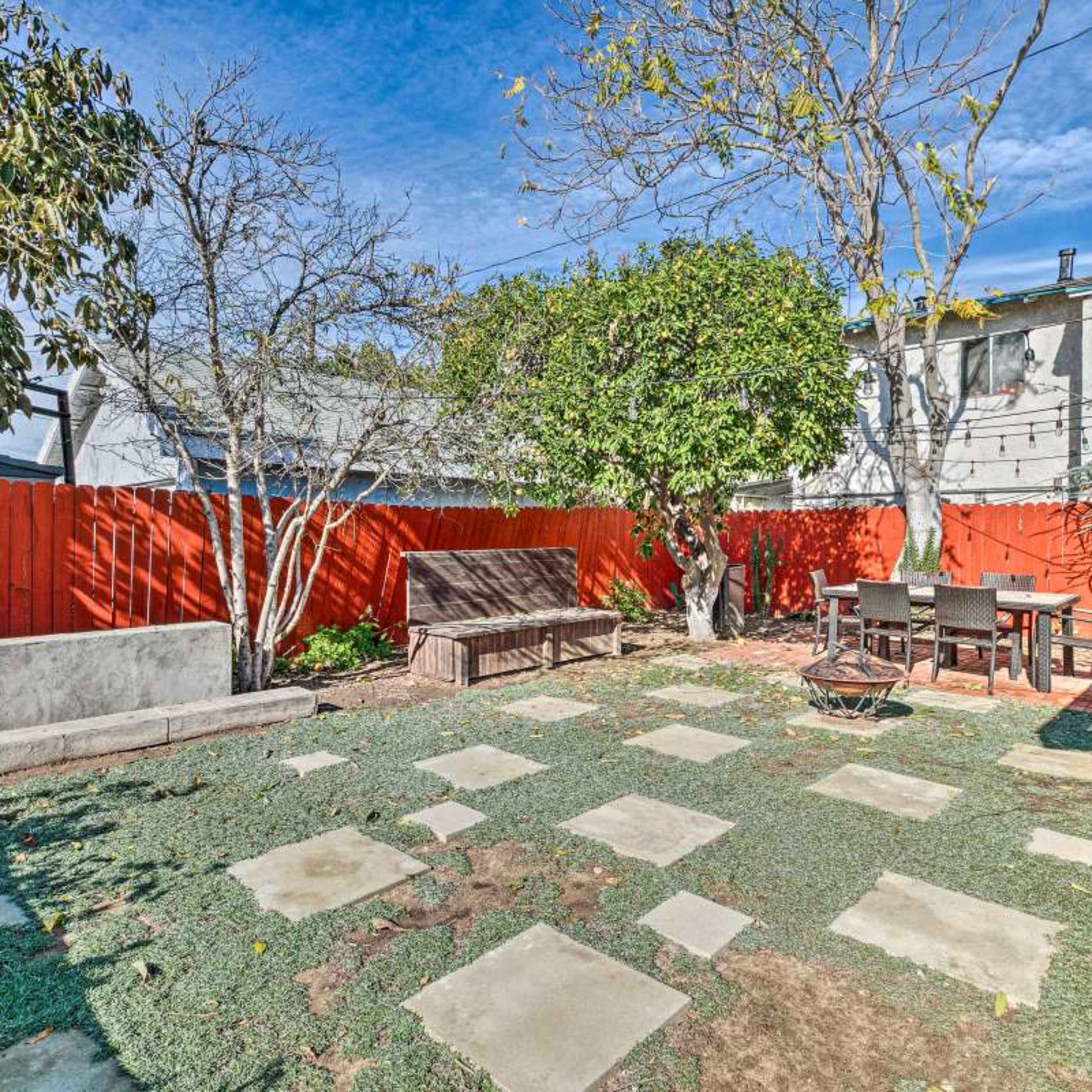 The backyard features a red wooden fence, a seating area with a table and chairs, a fire pit, and stone pavers on the ground.