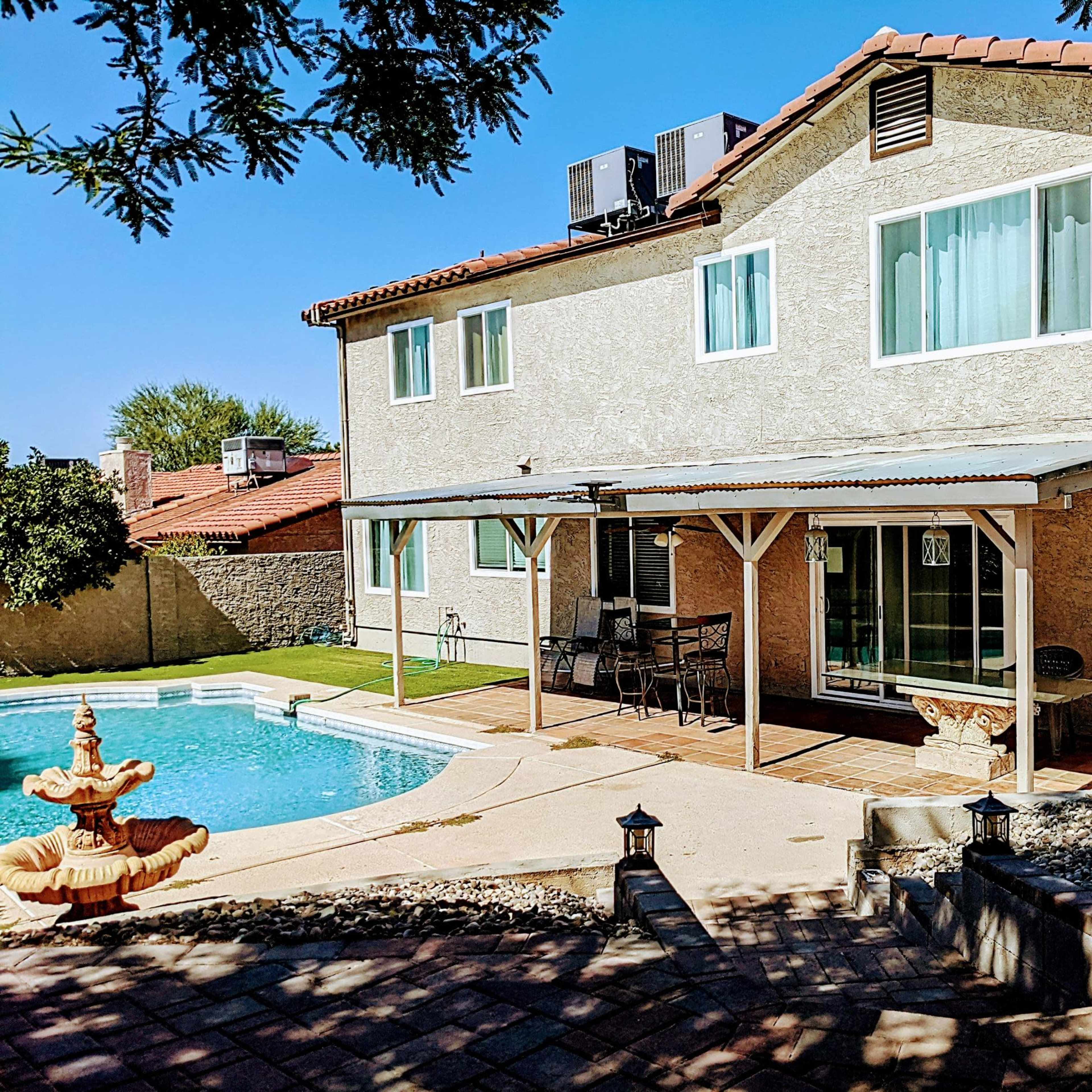 A two-story house with a patio, a swimming pool, and a stone fountain in a backyard setting.