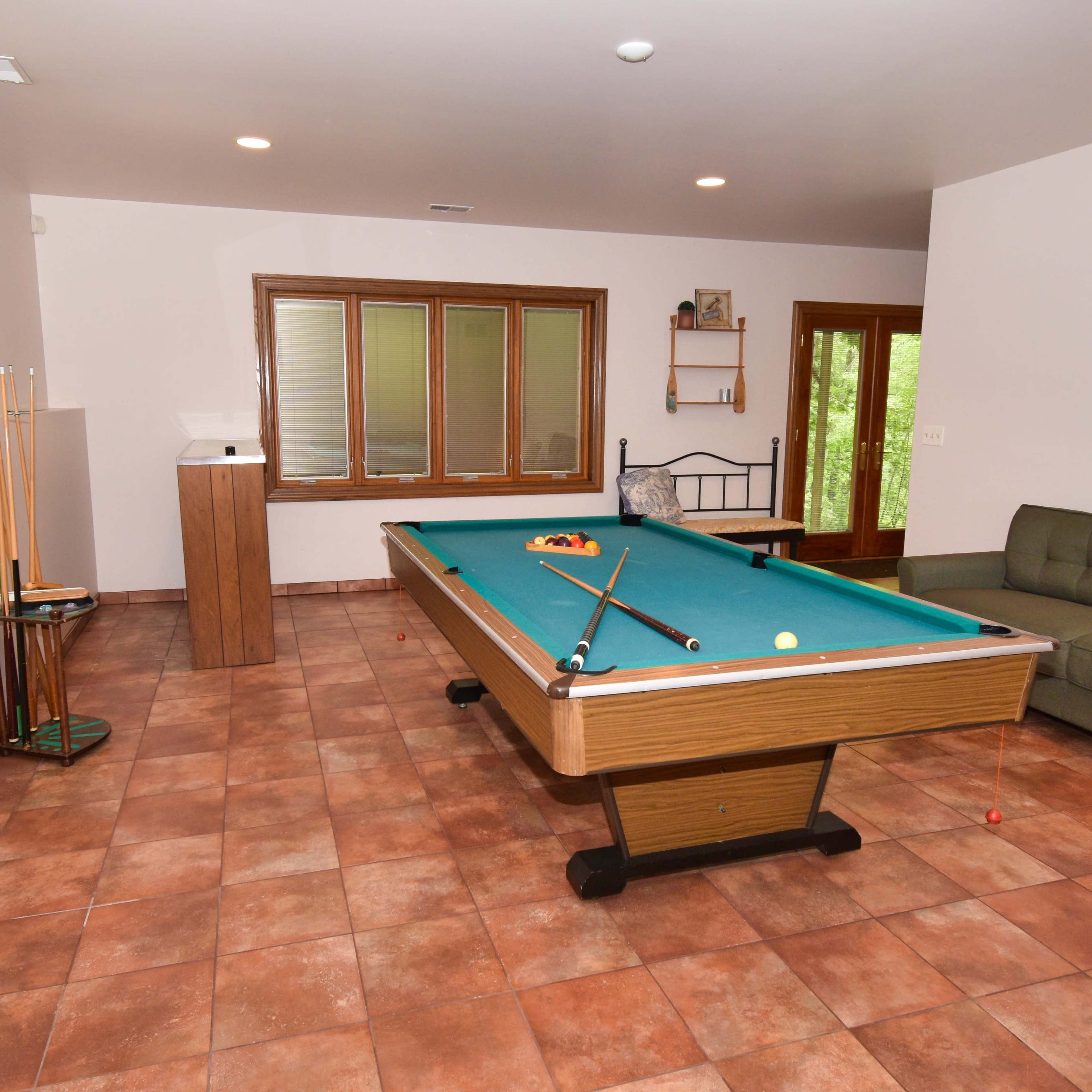 A game room with a pool table, a green couch, and tiled flooring.