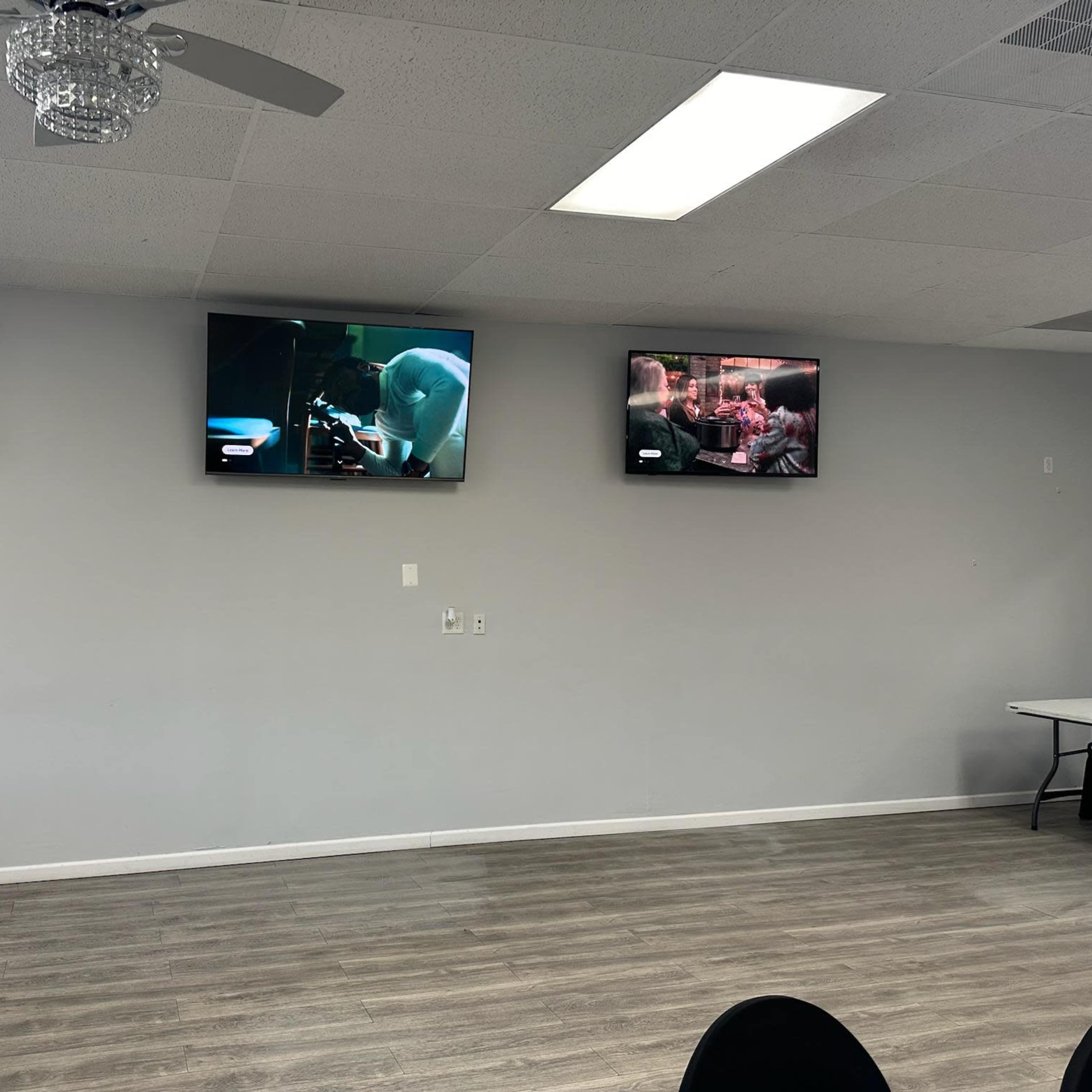 Three television screens are mounted on a light gray wall, each displaying different scenes from various shows or movies.