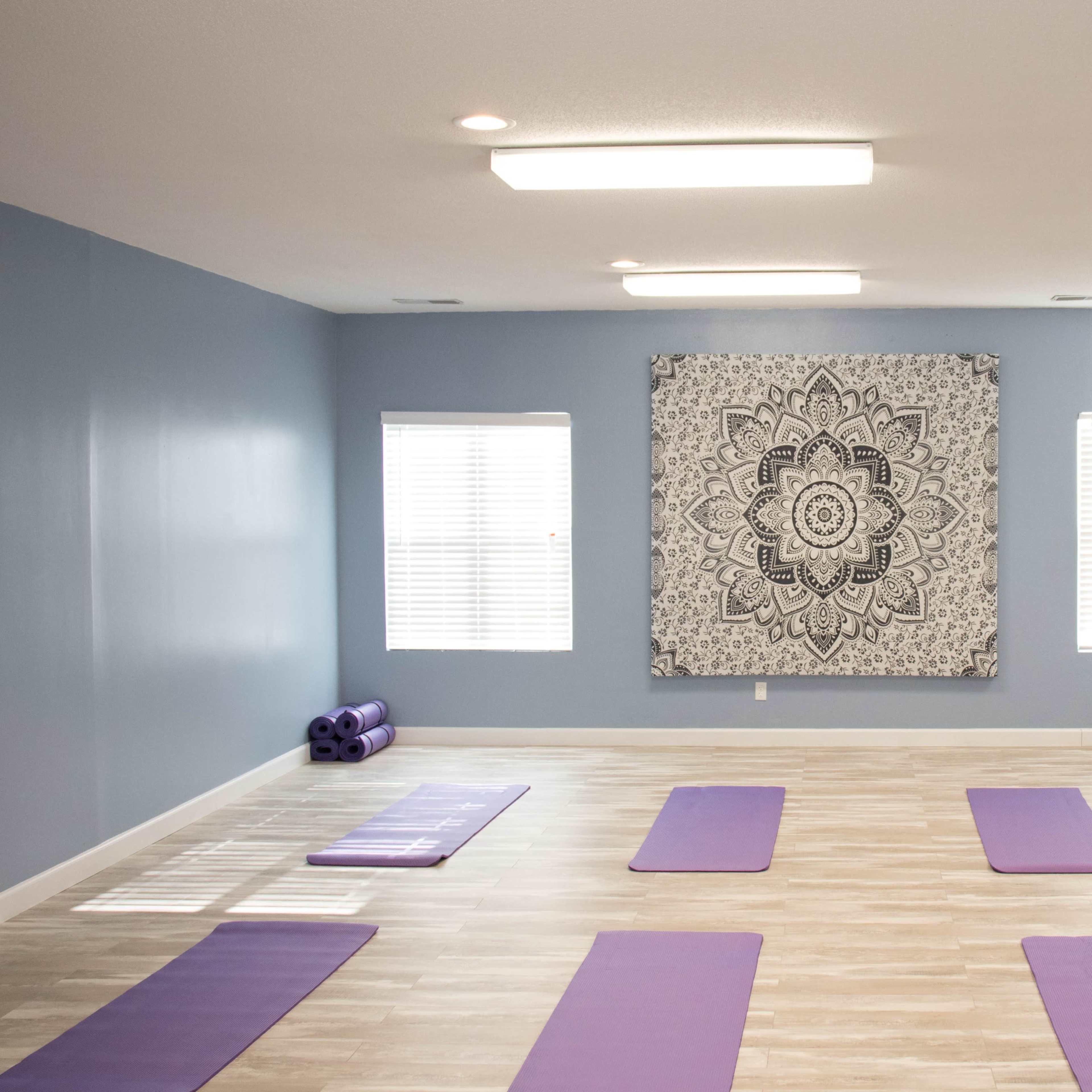A spacious yoga studio with several purple mats arranged on a wooden floor and a large mandala tapestry on the blue wall.