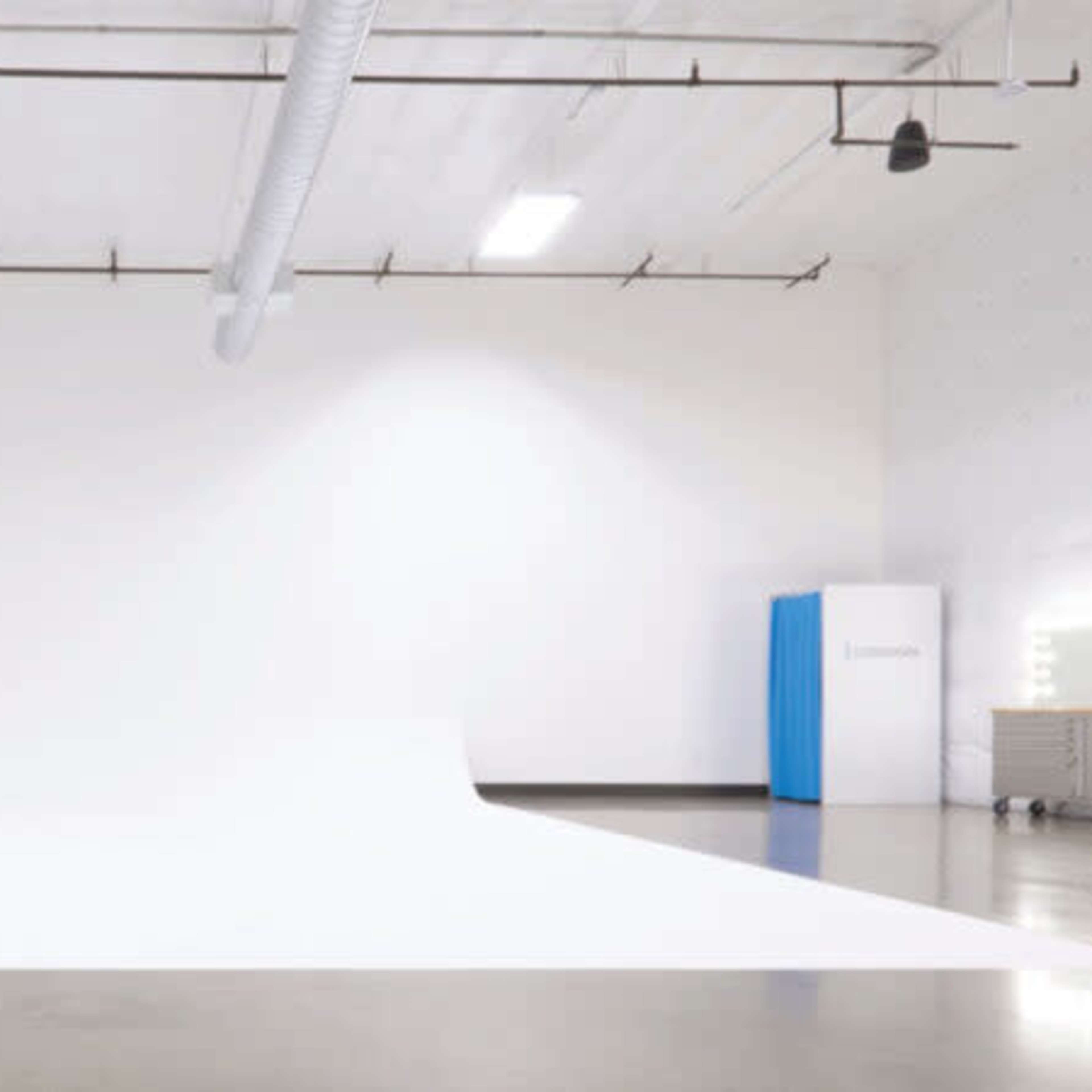 A spacious studio features a seamless white backdrop extending onto the floor, with a mirror and light setup in the corner.