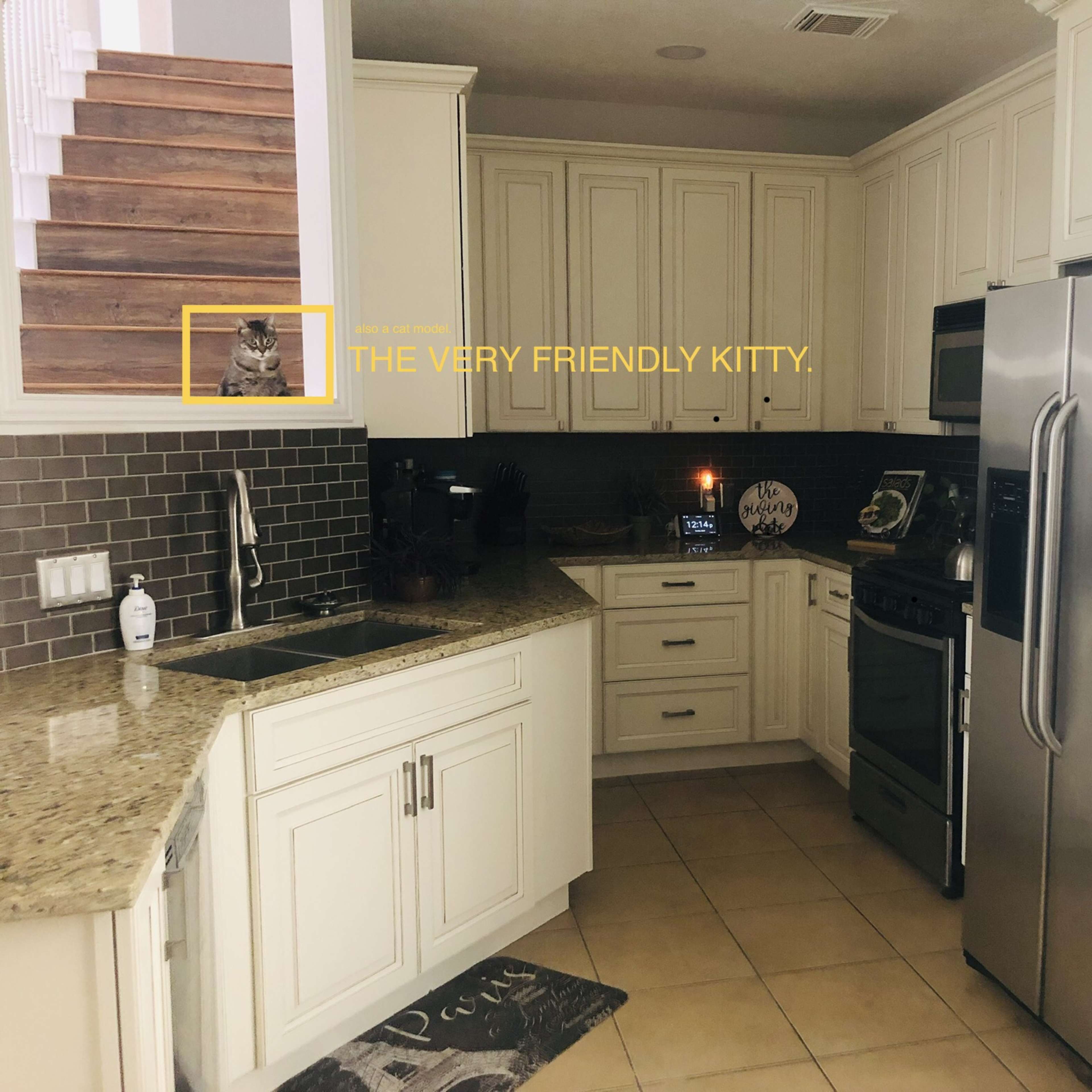 A modern kitchen features granite countertops, stainless steel appliances, and a view of a staircase in the background.
