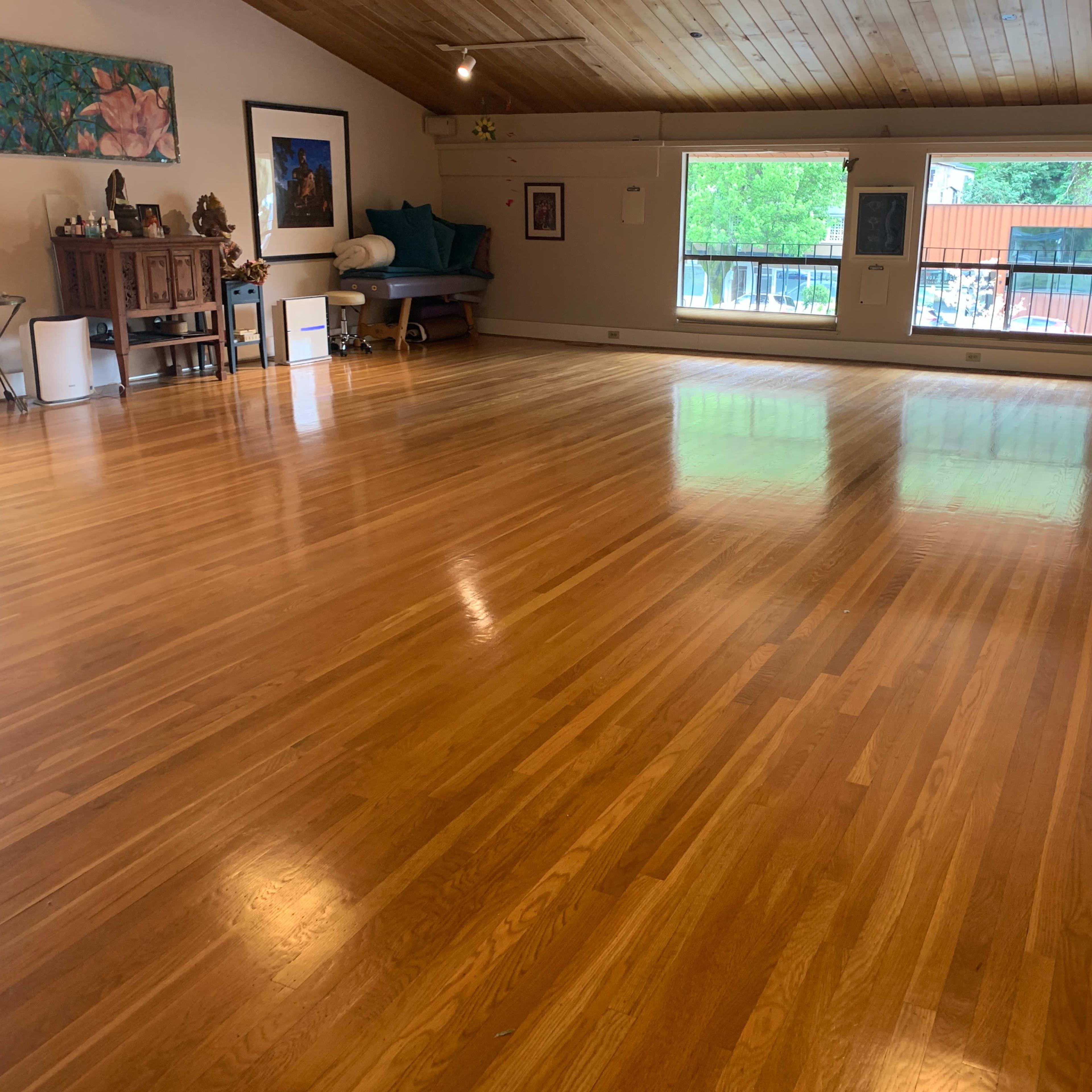 A spacious wooden-floored room with large windows and minimal furniture.