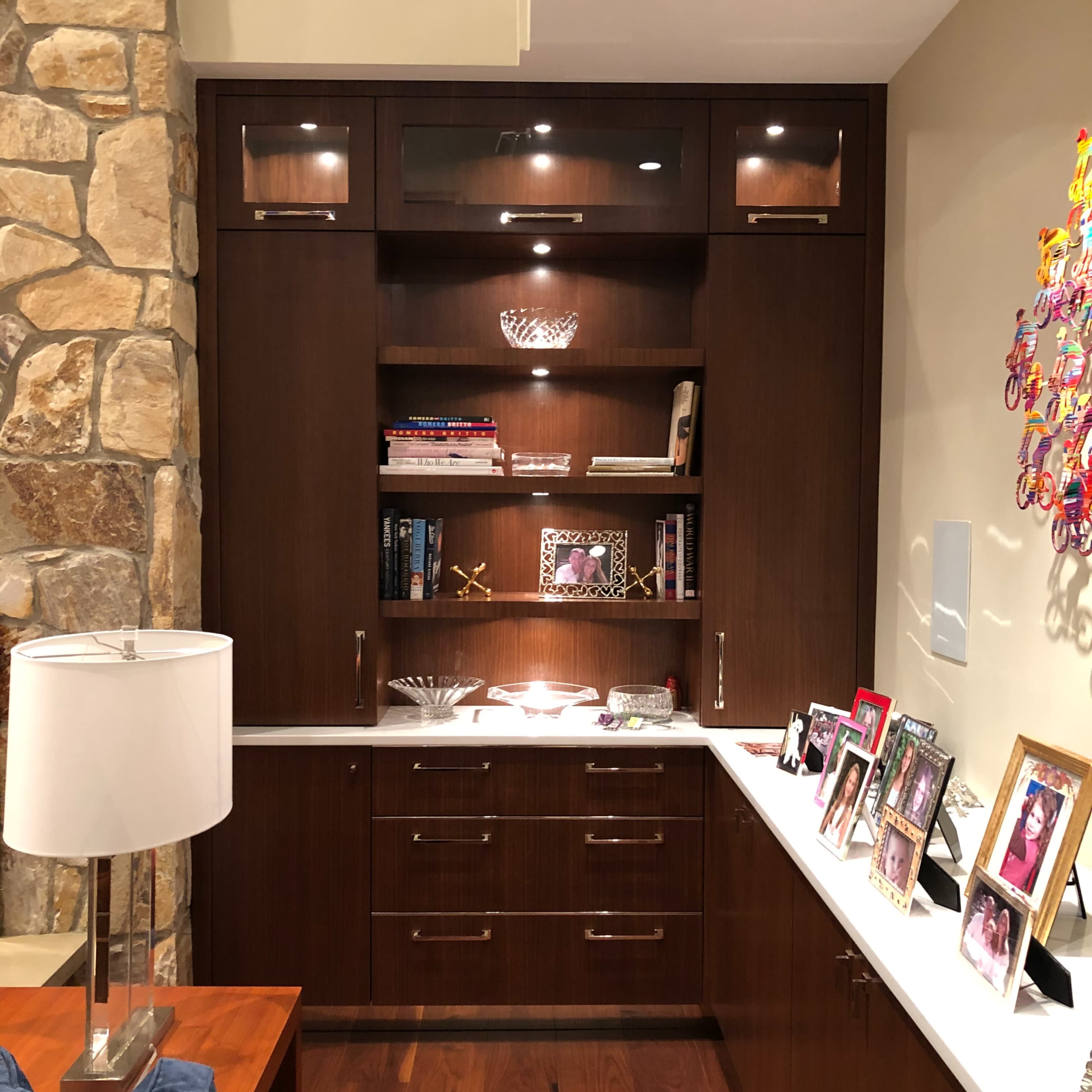 A wooden wall unit with shelves displaying books and decorative items, set against a stone wall, next to a couch and a lamp.