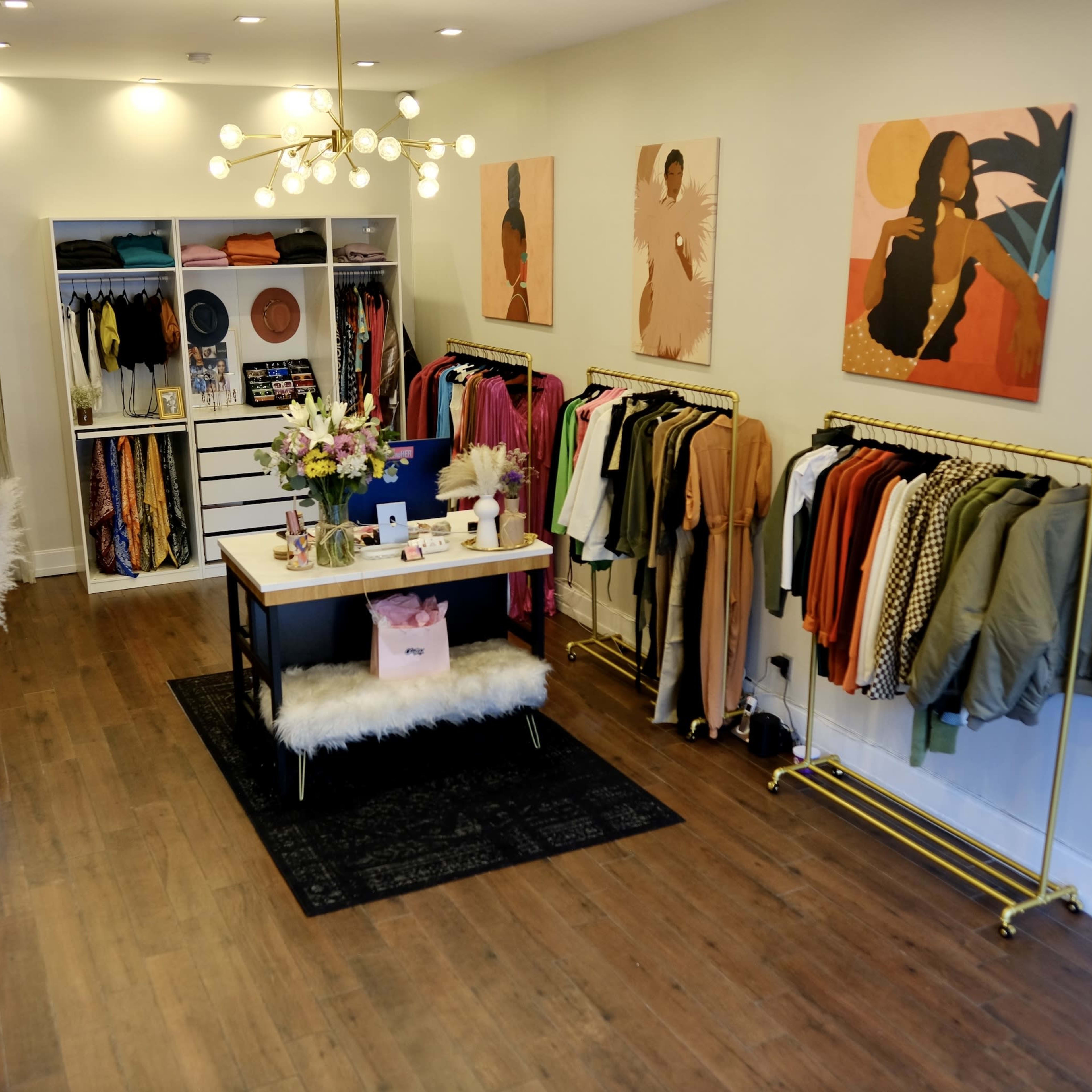 A boutique storefront featuring clothing racks, a central display table with flowers, and artwork on the walls.