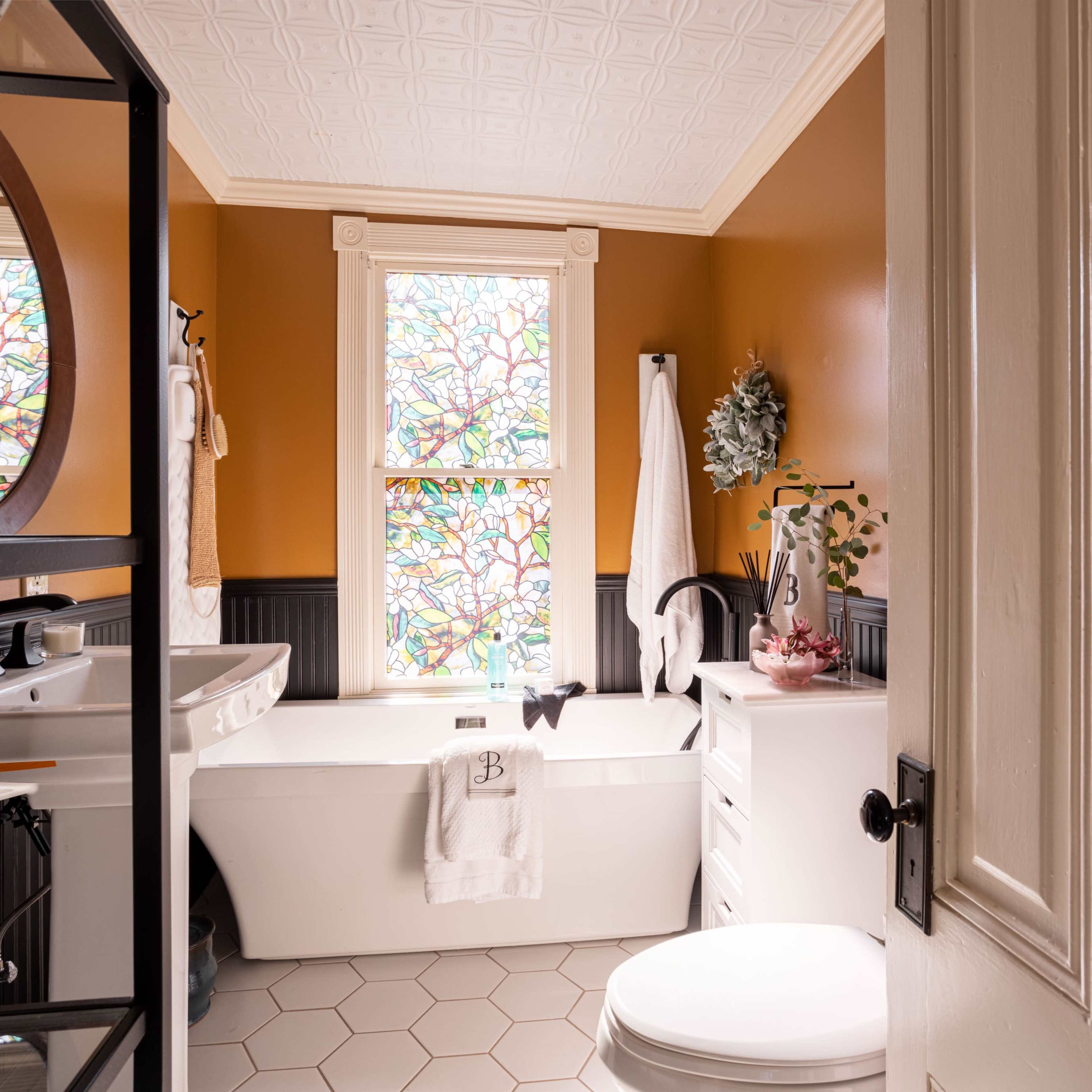 A bathroom featuring a freestanding bathtub, decorative stained glass windows, and a combination of orange and dark wall paneling.