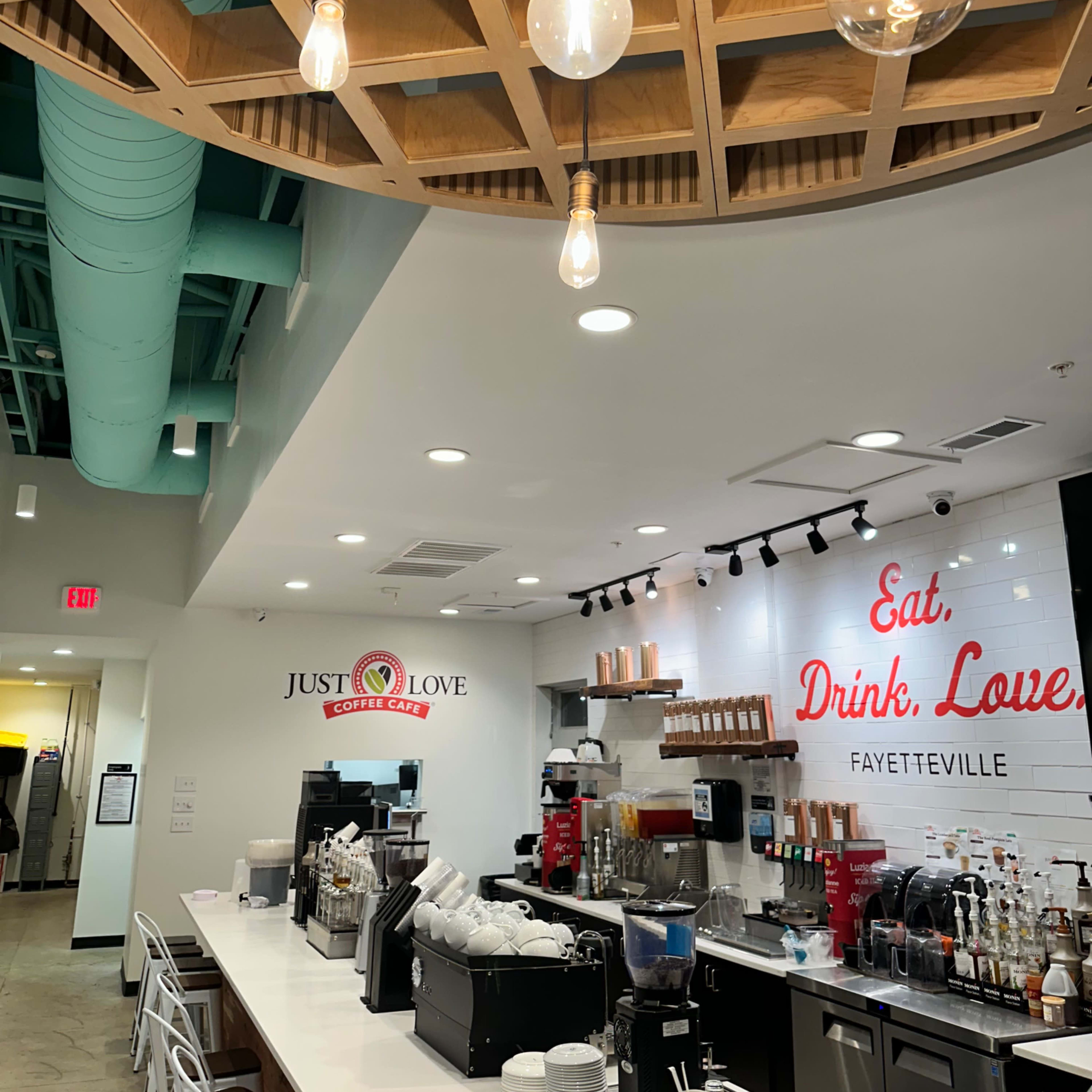 The interior of a coffee shop with a modern design, featuring a long counter with coffee equipment and a bright chandelier overhead.