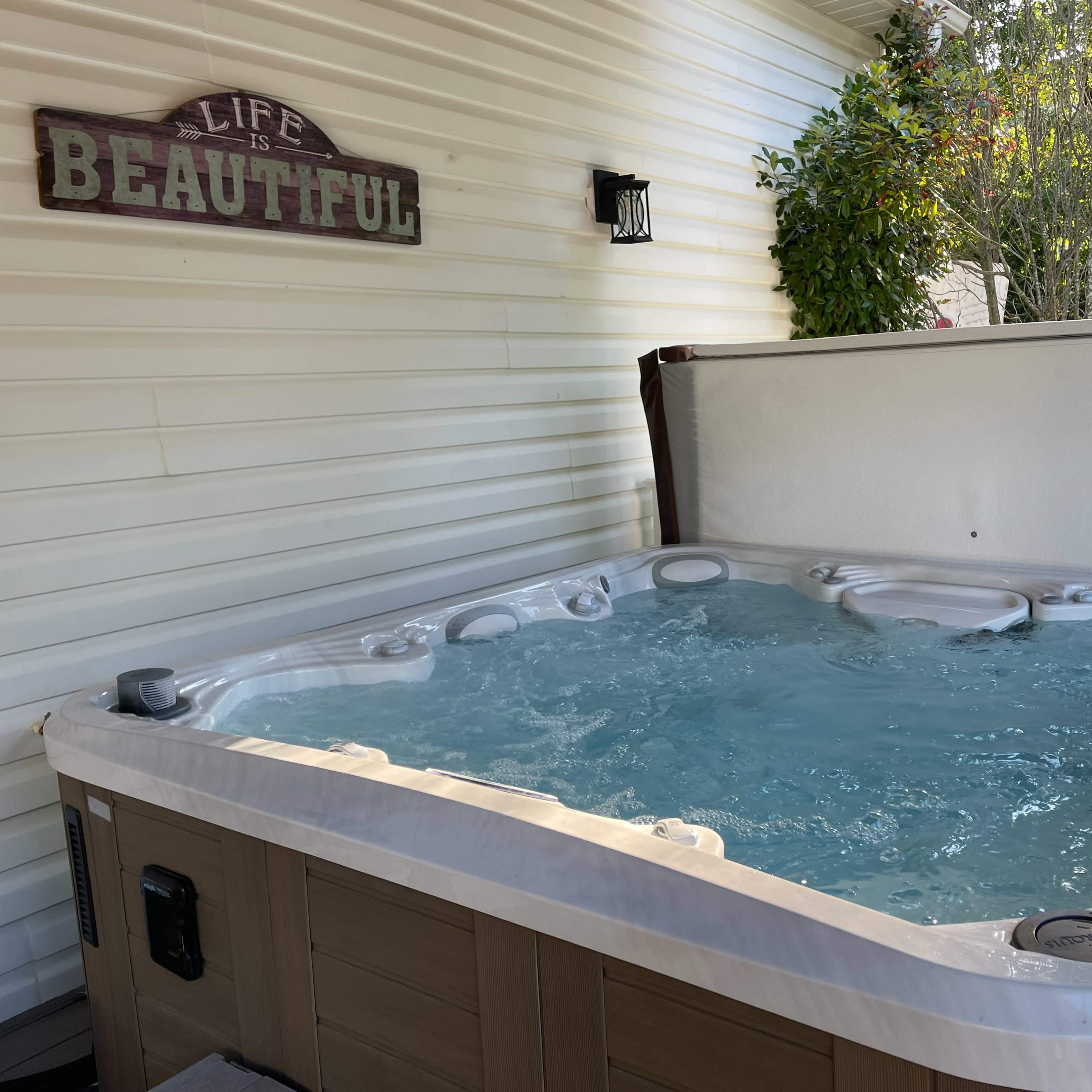 A hot tub with bubbling water is situated against a white wall adorned with a sign that reads "LIFE BEAUTIFUL."