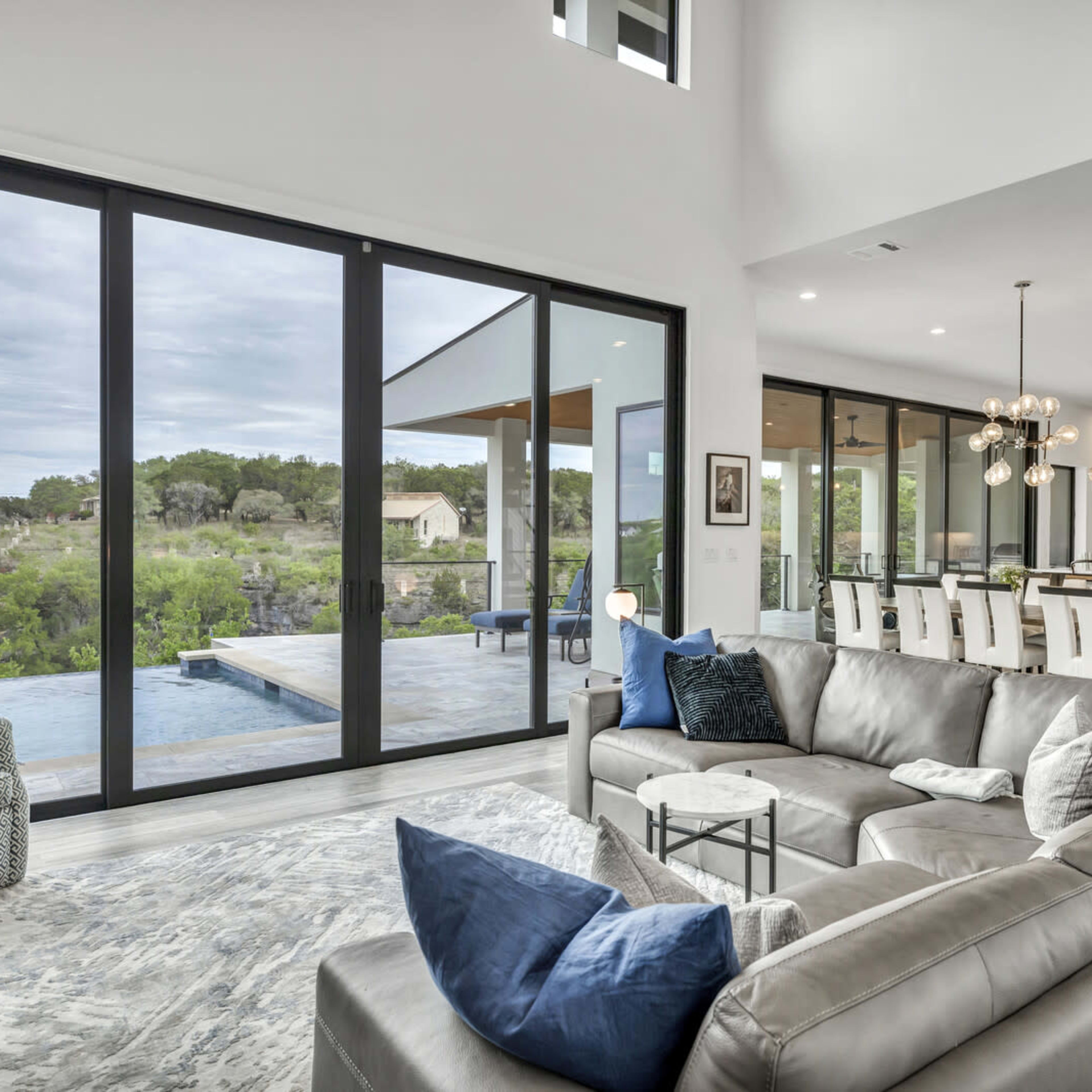 A modern living room with large windows overlooking a green landscape and a pool area.