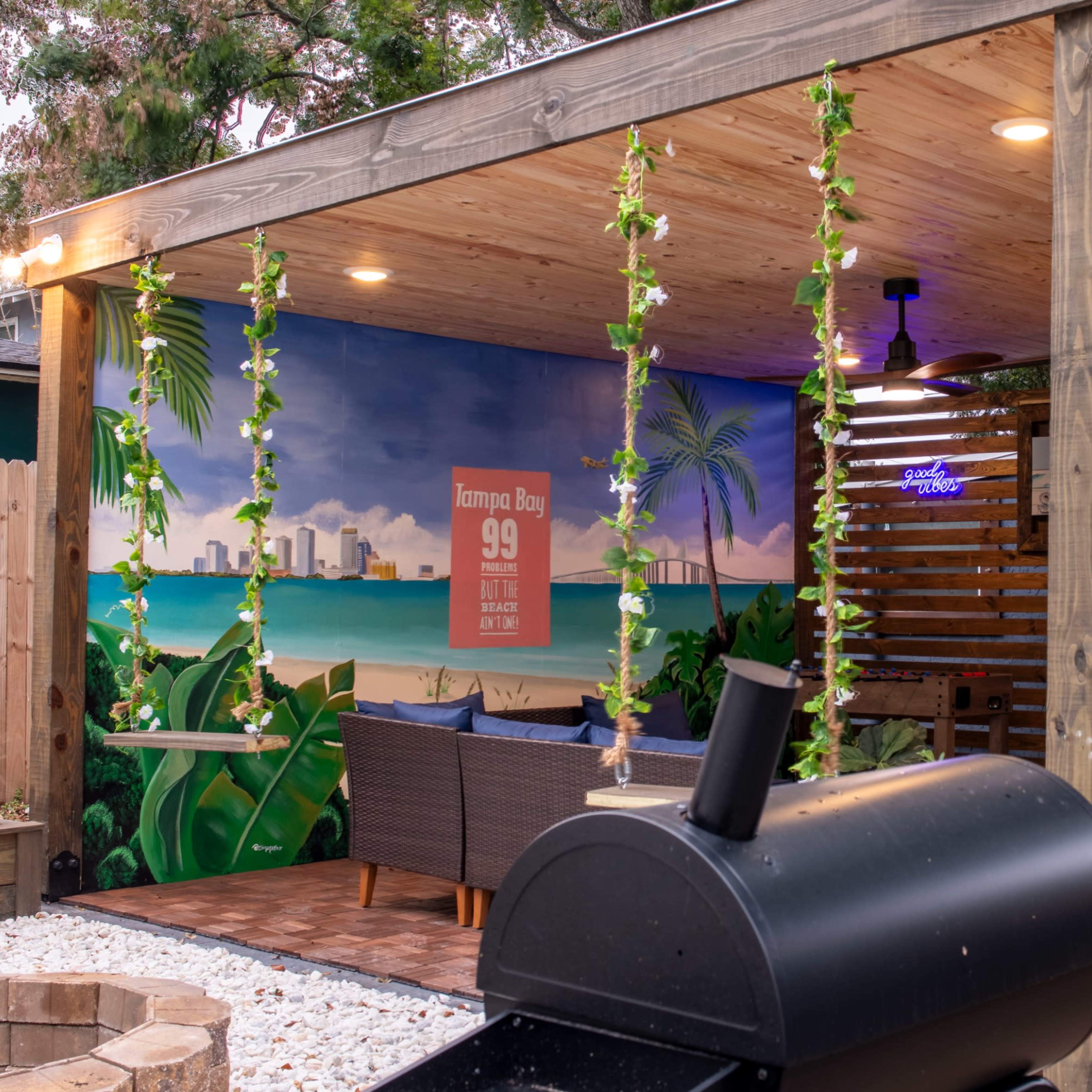 A spacious outdoor patio area with a wooden structure, string lights, and seating surrounded by greenery.