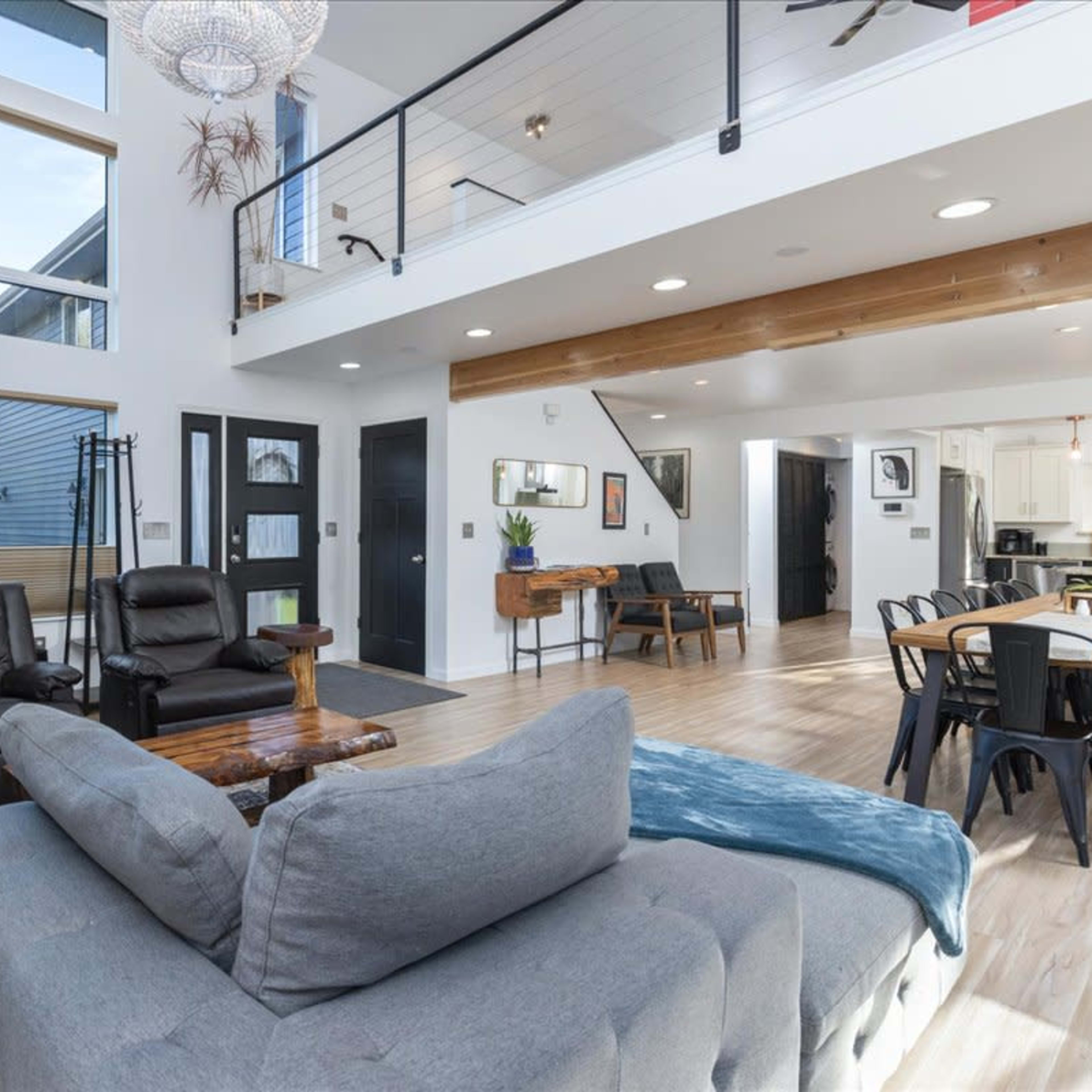A modern, open-concept living area featuring a comfortable seating arrangement, large windows, and a dining area in a well-lit space.