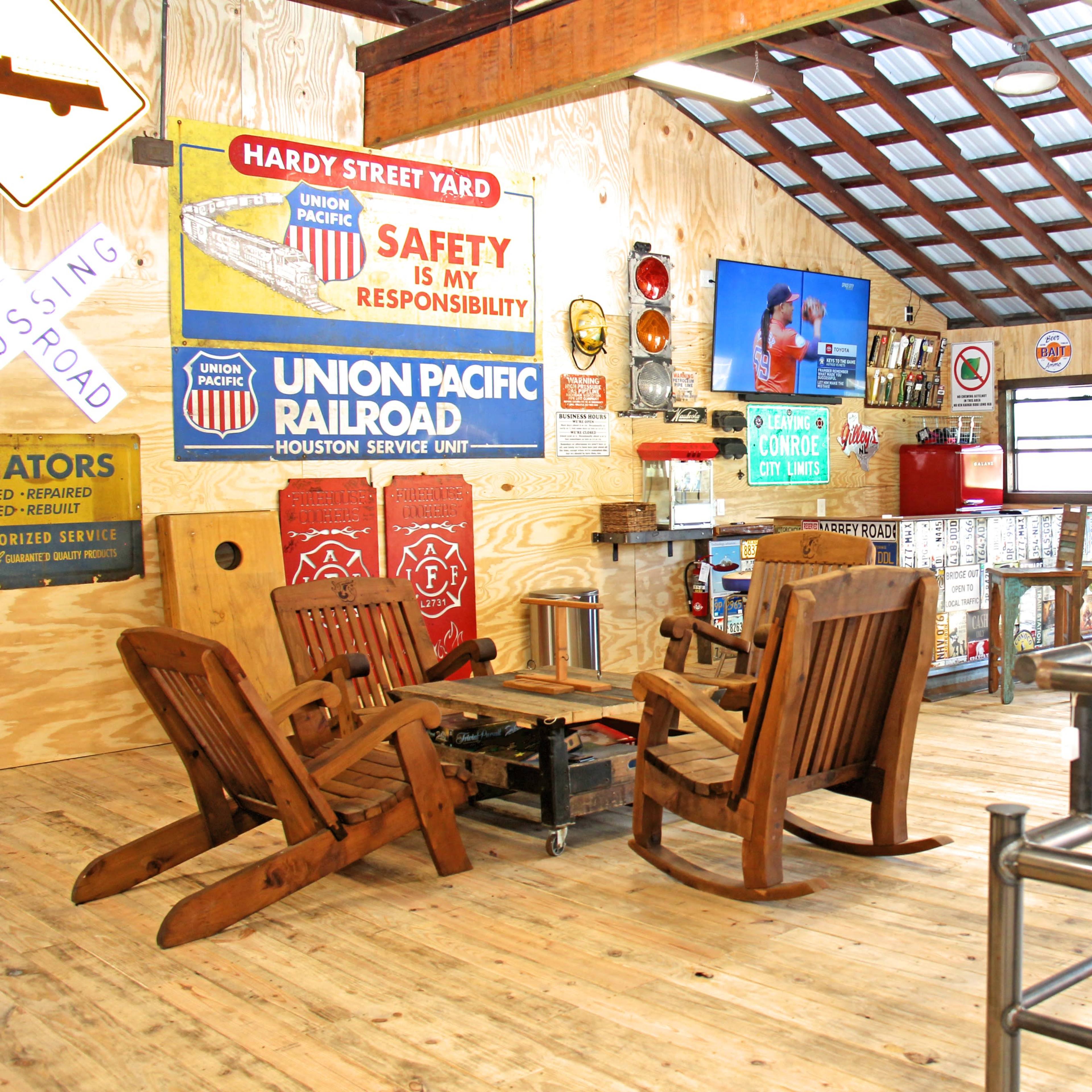A rustic interior with wooden rocking chairs and a coffee table, adorned with vintage railroad and safety signs on the walls.