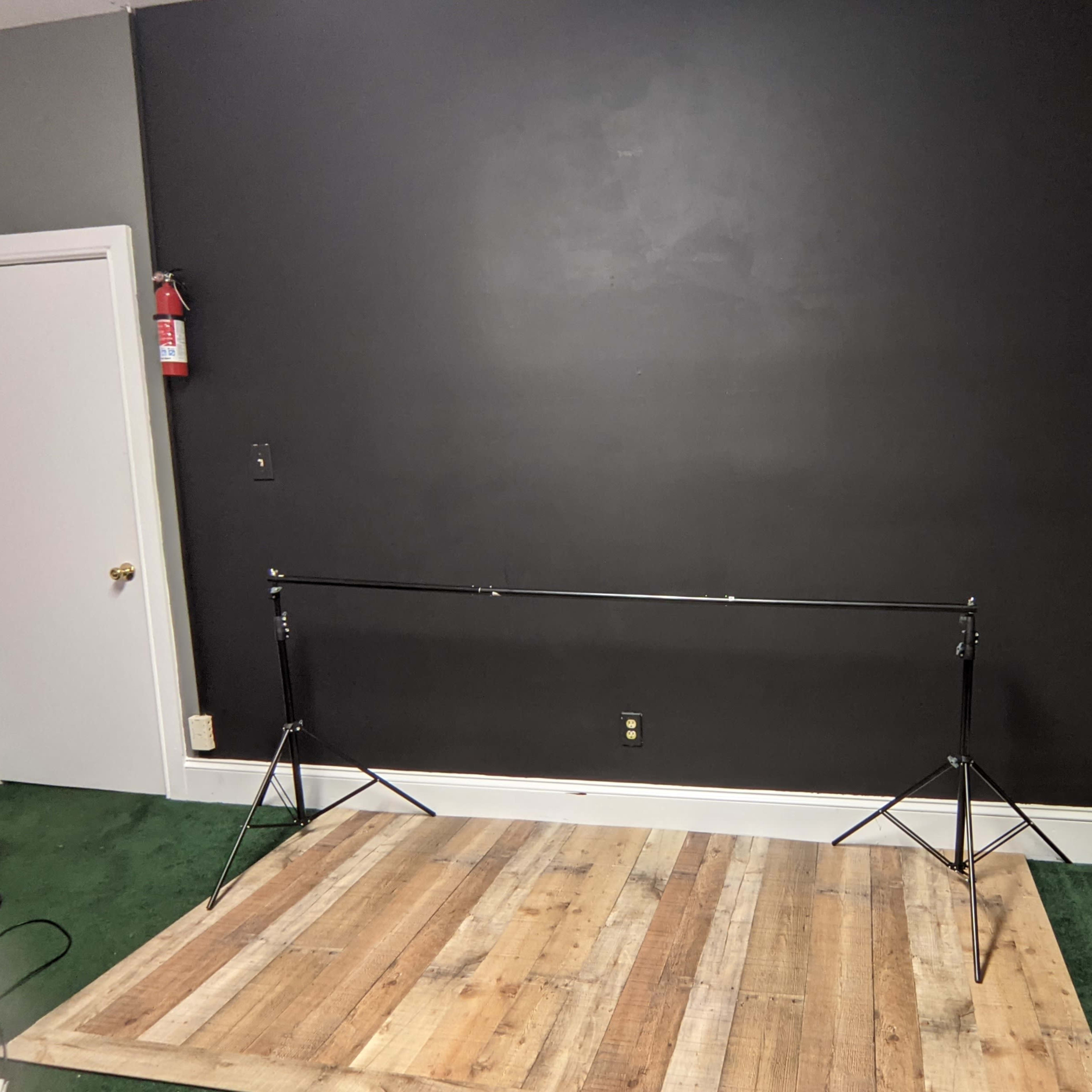 A minimalist setting with a wooden platform in front of a black wall, supported by two metal stands on either side.