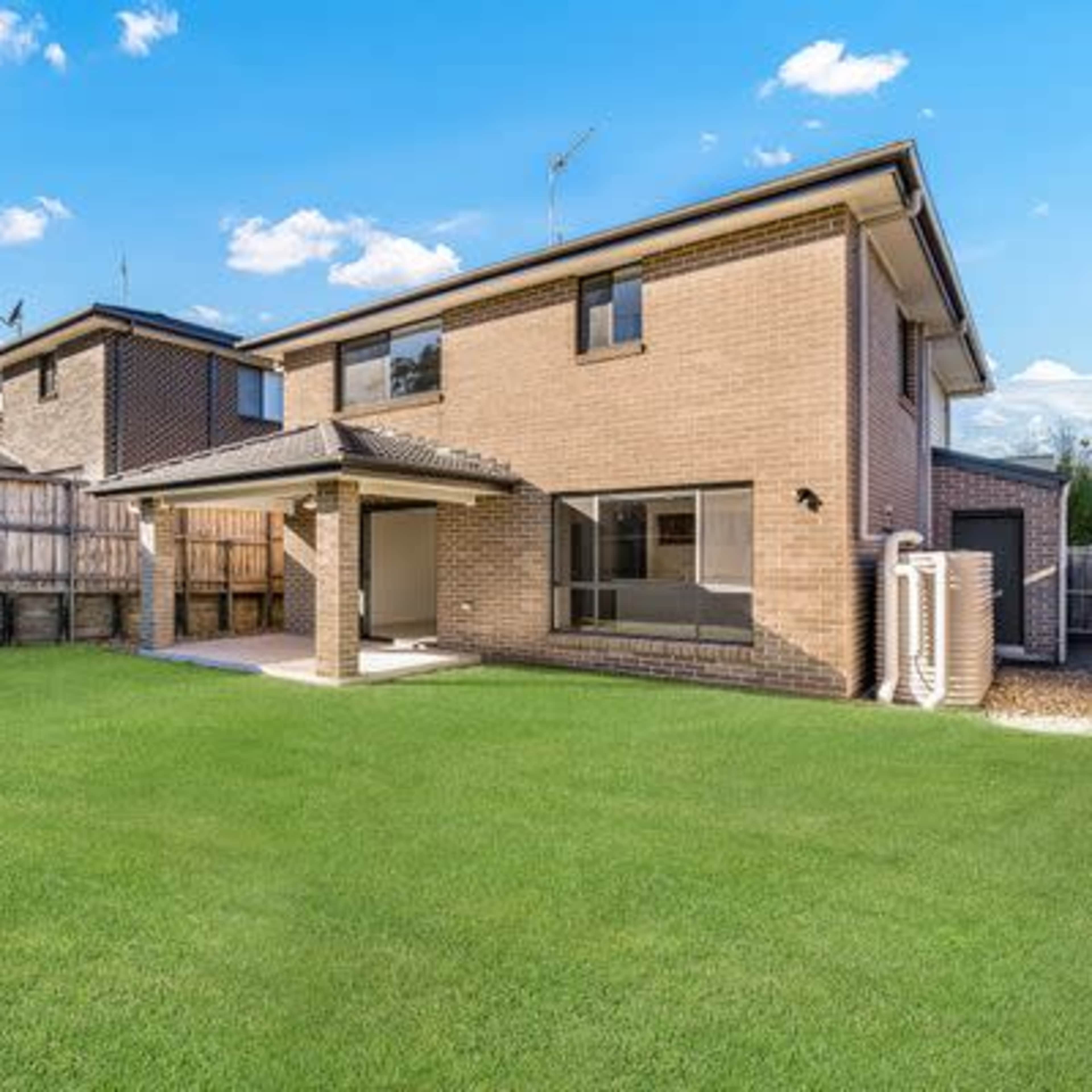 A two-story brick house with a neatly maintained lawn in the backyard, surrounded by wooden fencing.