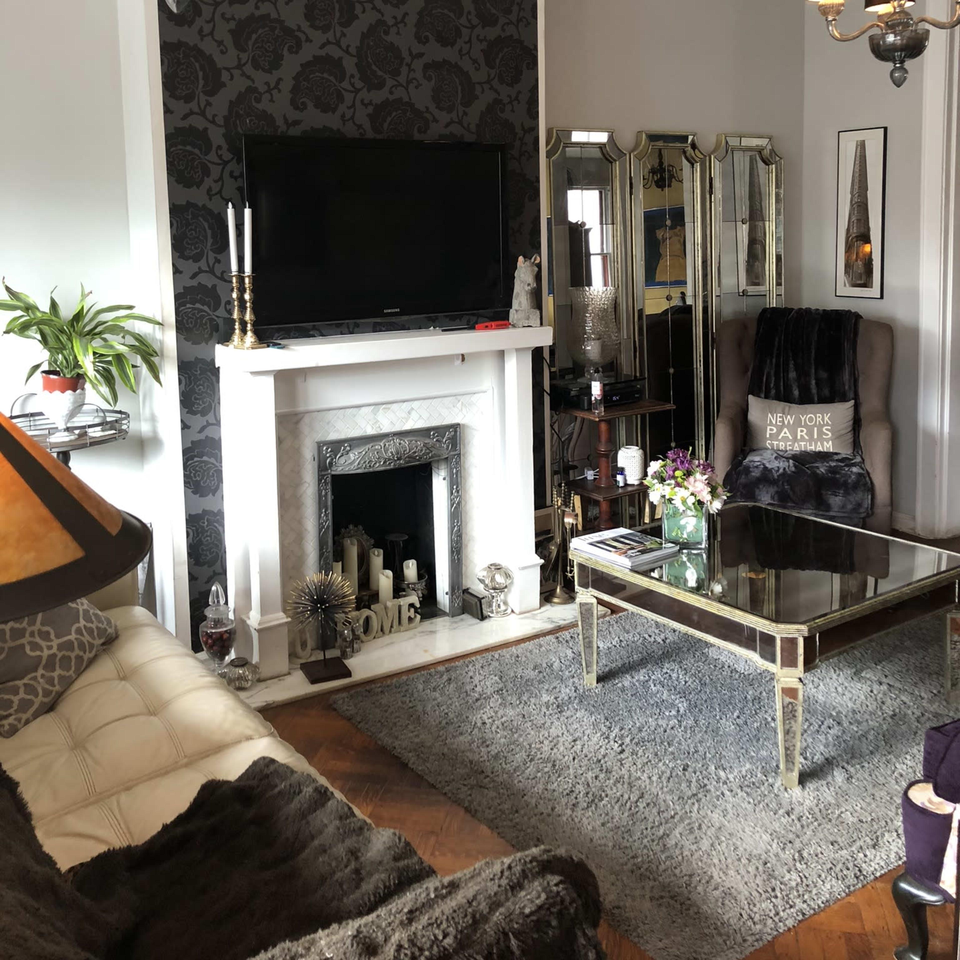 A stylish living room featuring a modern fireplace, a large flat-screen TV, and a mirrored coffee table, with decorative elements including candles and plants.