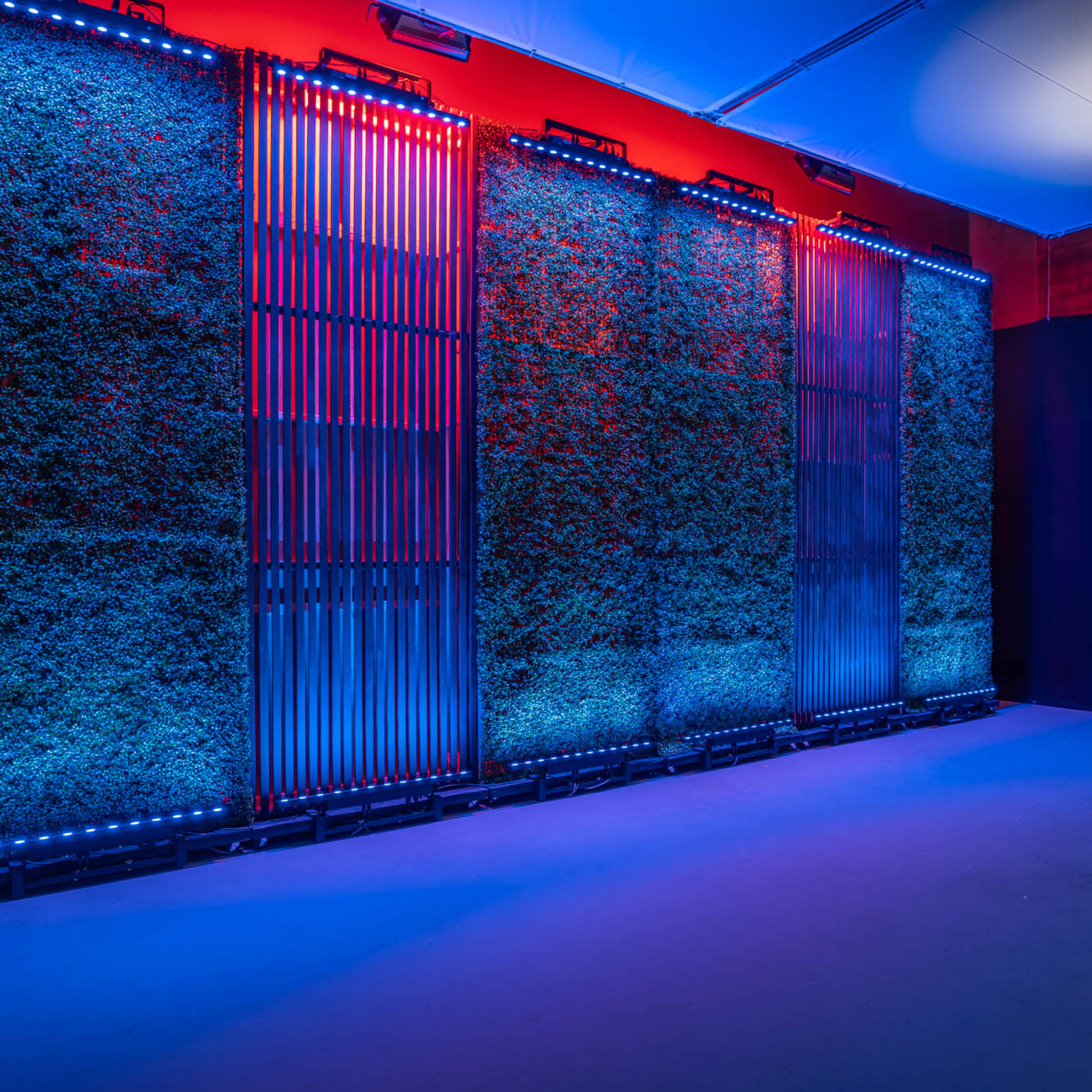 Three vertical panels covered in greenery, illuminated with blue and red lights in a dimly lit room.