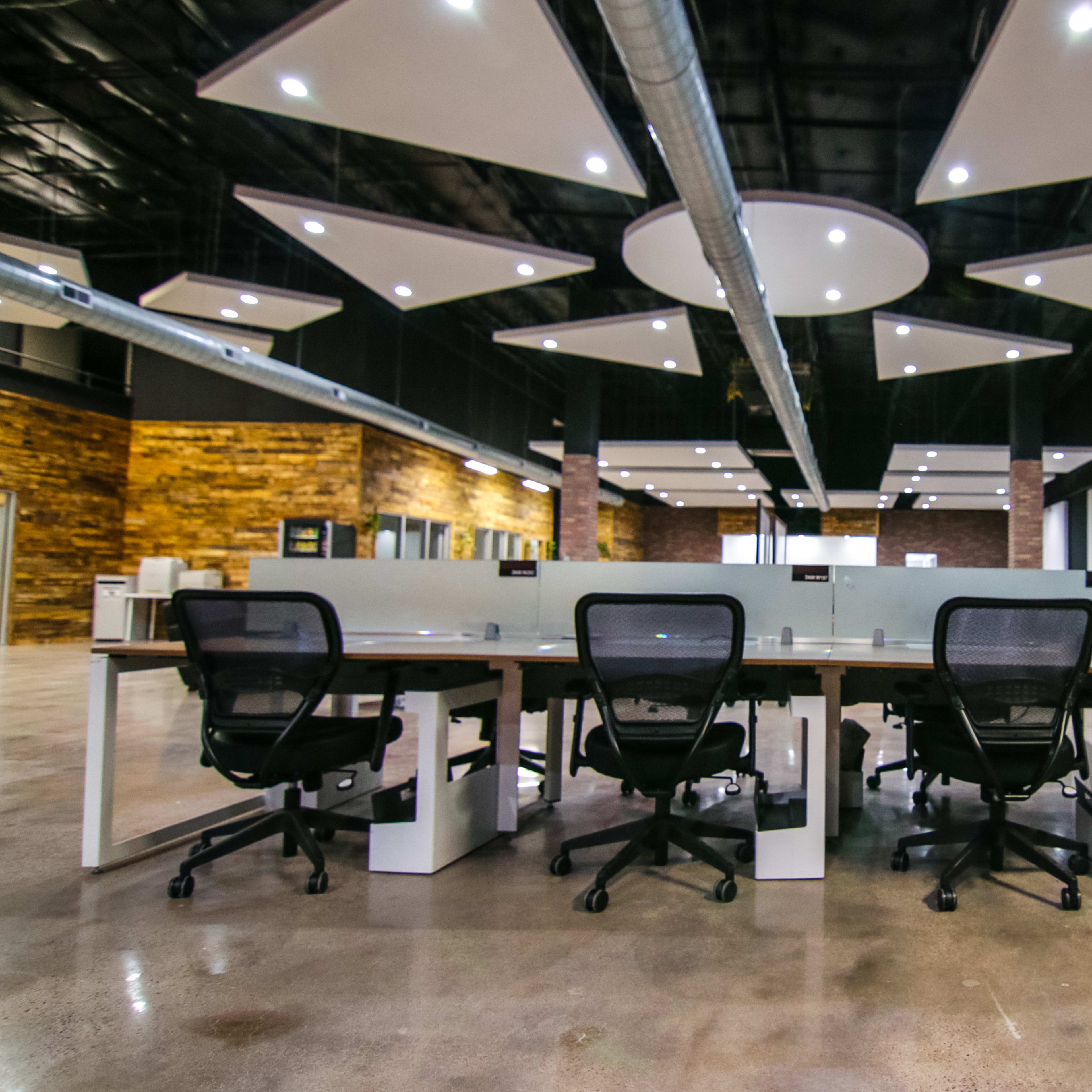 A modern office space features rows of desks with ergonomic chairs and exposed brick walls, illuminated by overhead lighting.