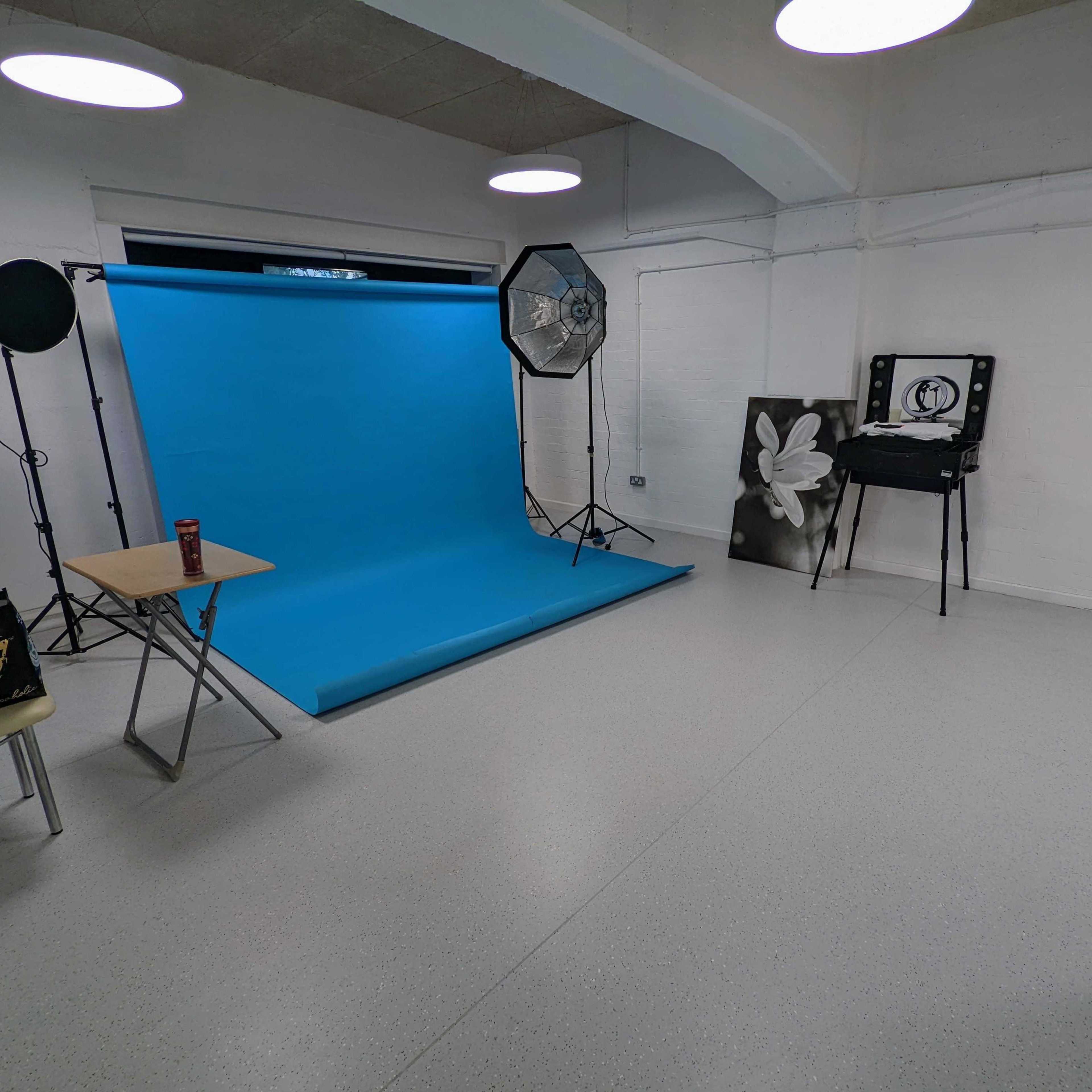 A photography studio with a blue backdrop, softbox lighting, and a table set up in a sparsely furnished room.