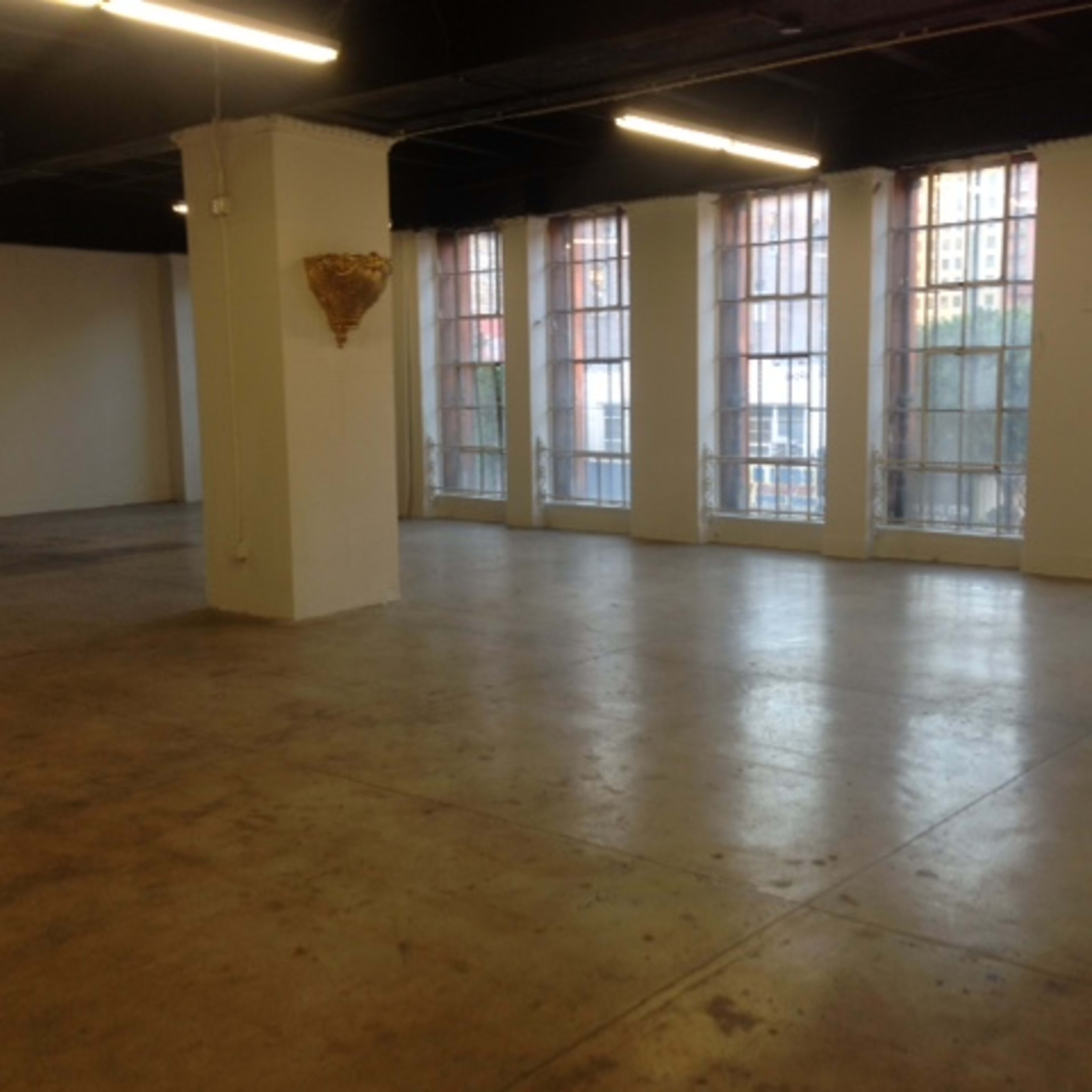 A large, empty room with concrete floors and large windows along one wall.