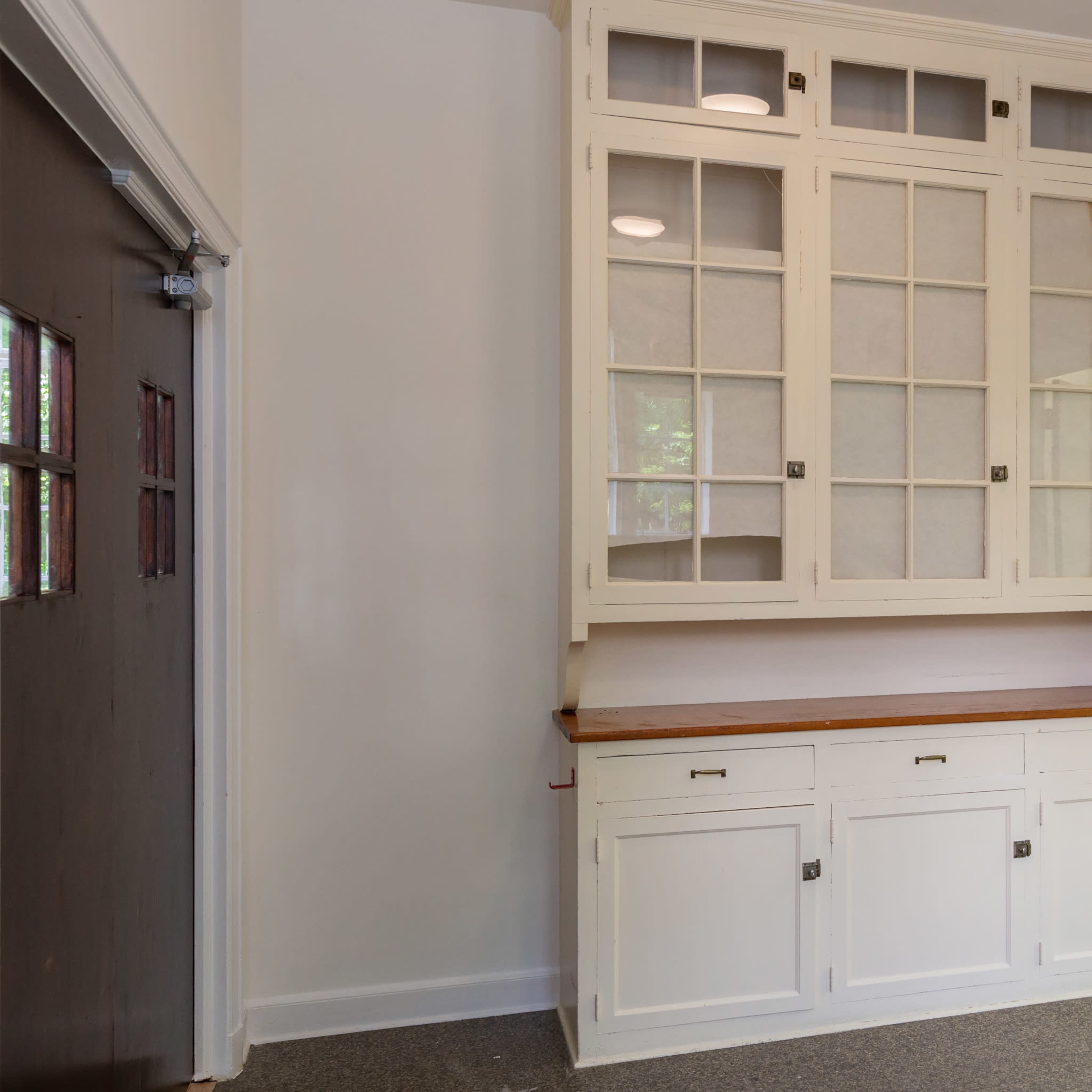 A white kitchen hutch with glass-fronted cabinets and a wooden countertop in a well-lit room.
