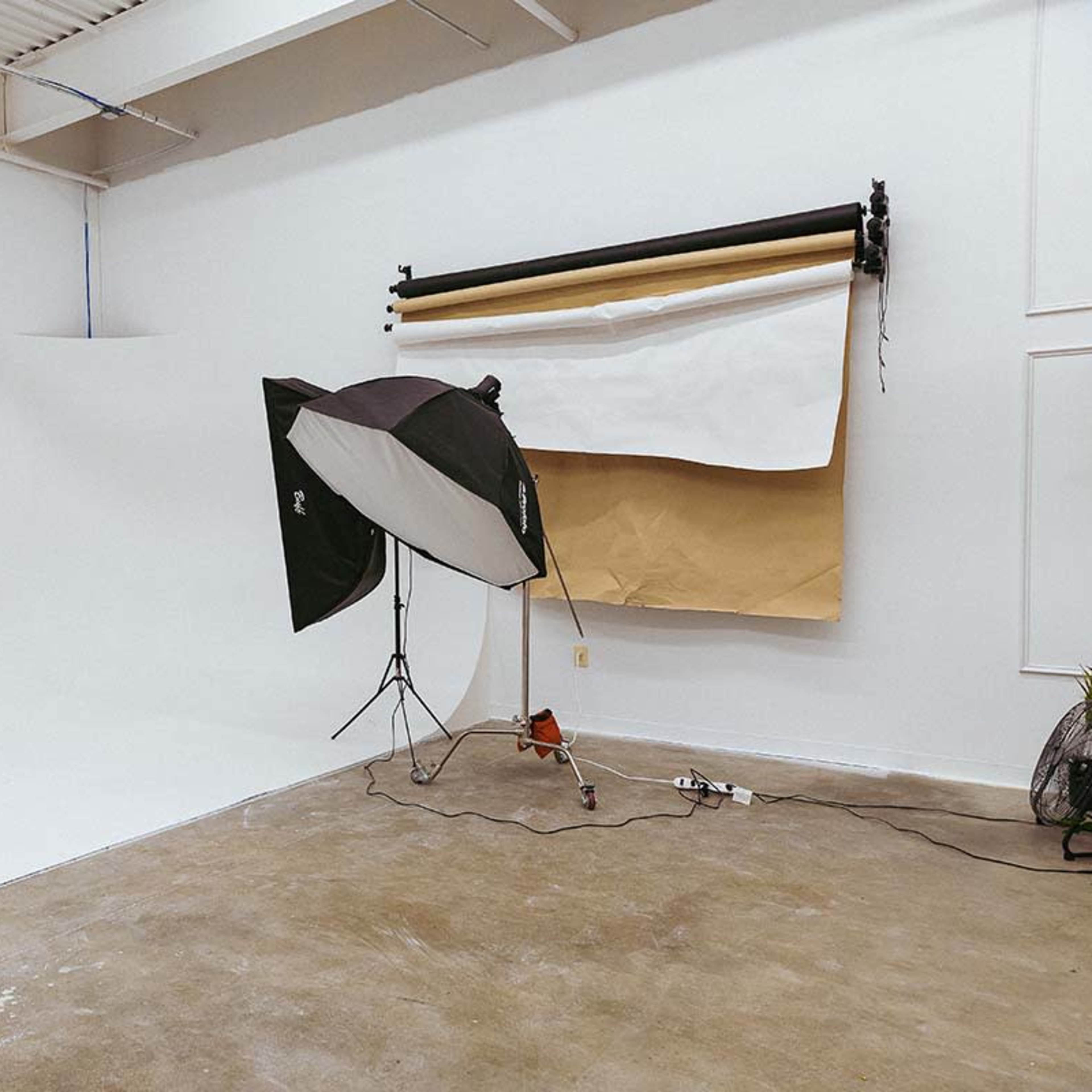 A photography studio features a white backdrop and two softbox light setups on a concrete floor.
