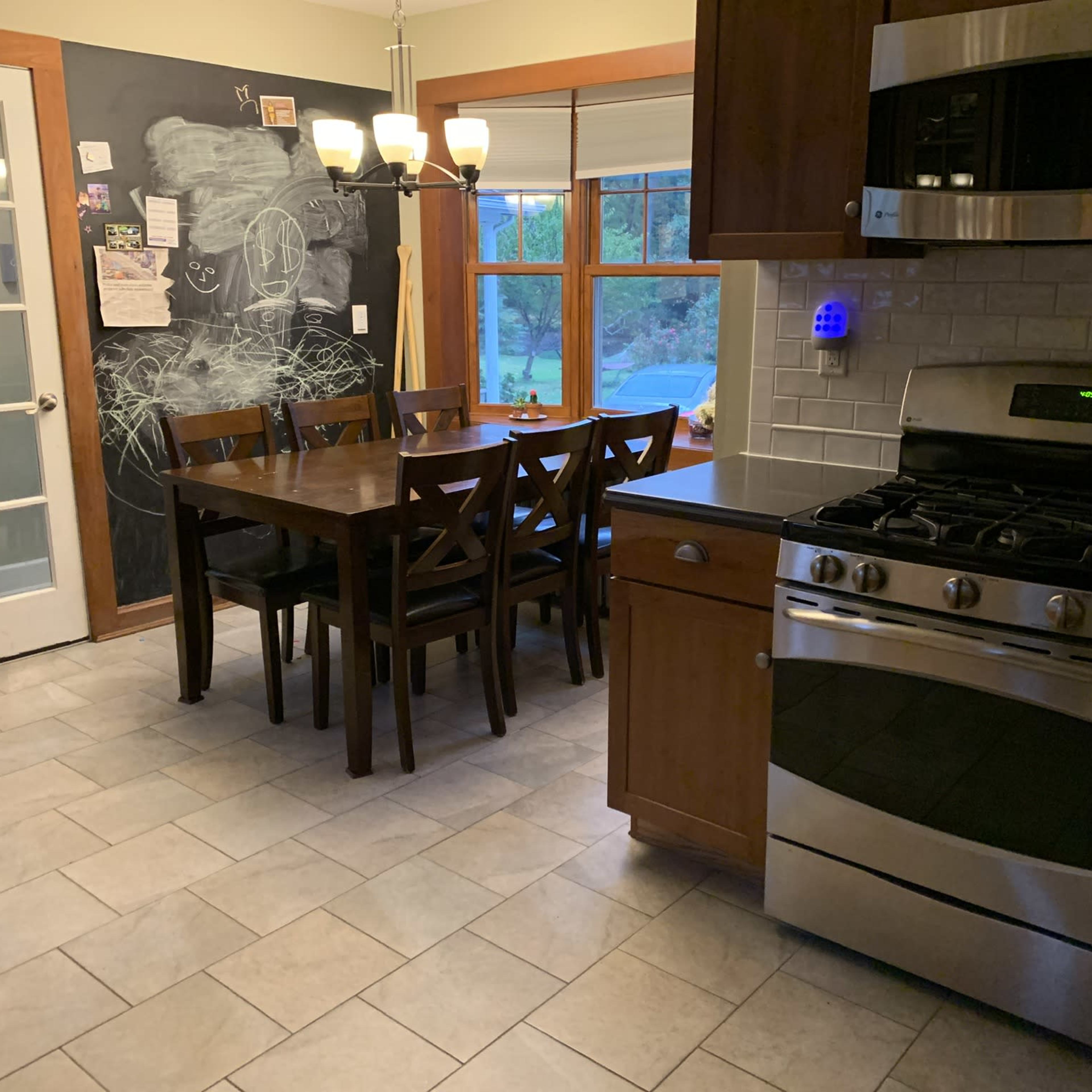 A kitchen with a dining table and chairs, a stainless steel stove, and a chalkboard wall beside a window.