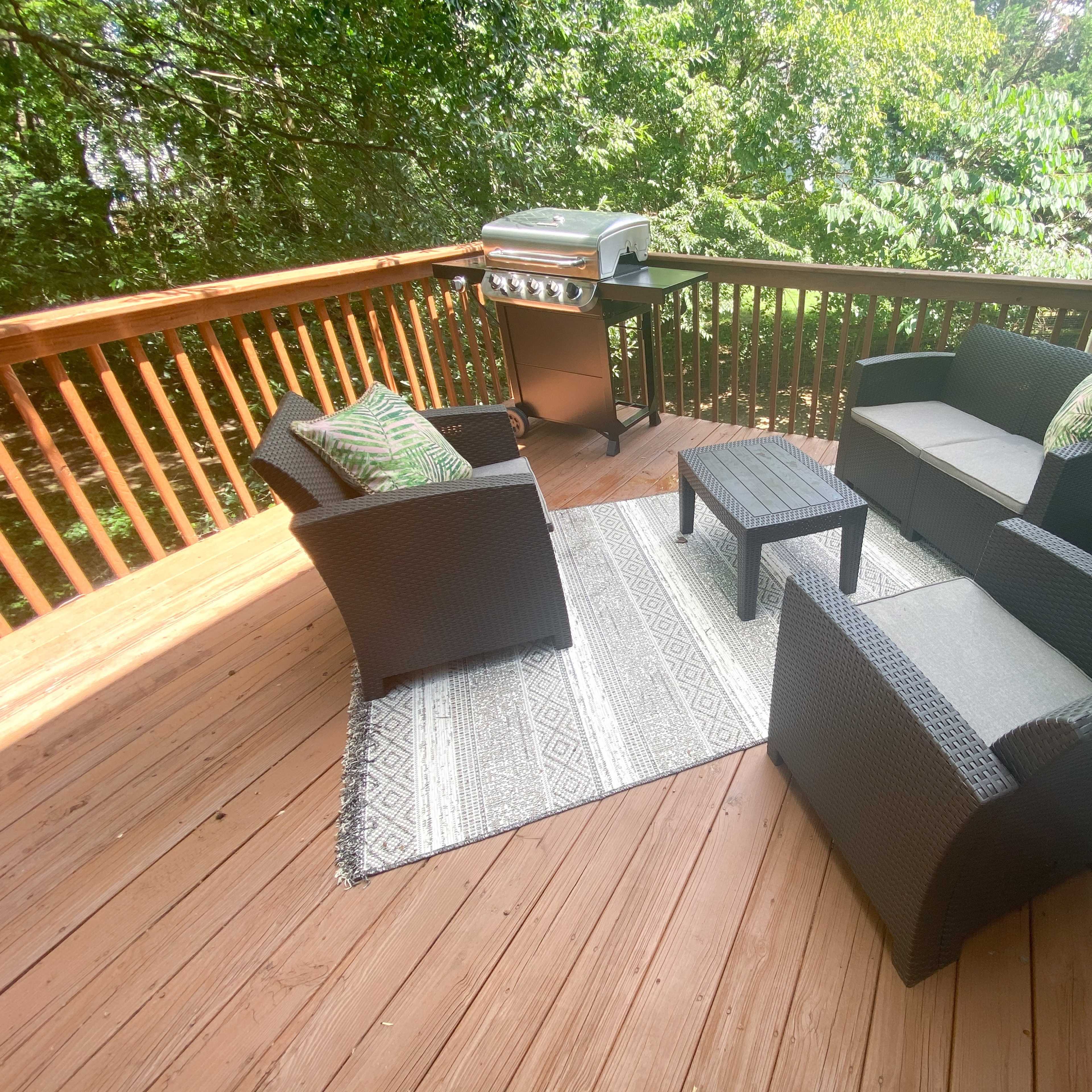 A deck features a seating area with two chairs, a loveseat, and a coffee table, along with a grill in the background.