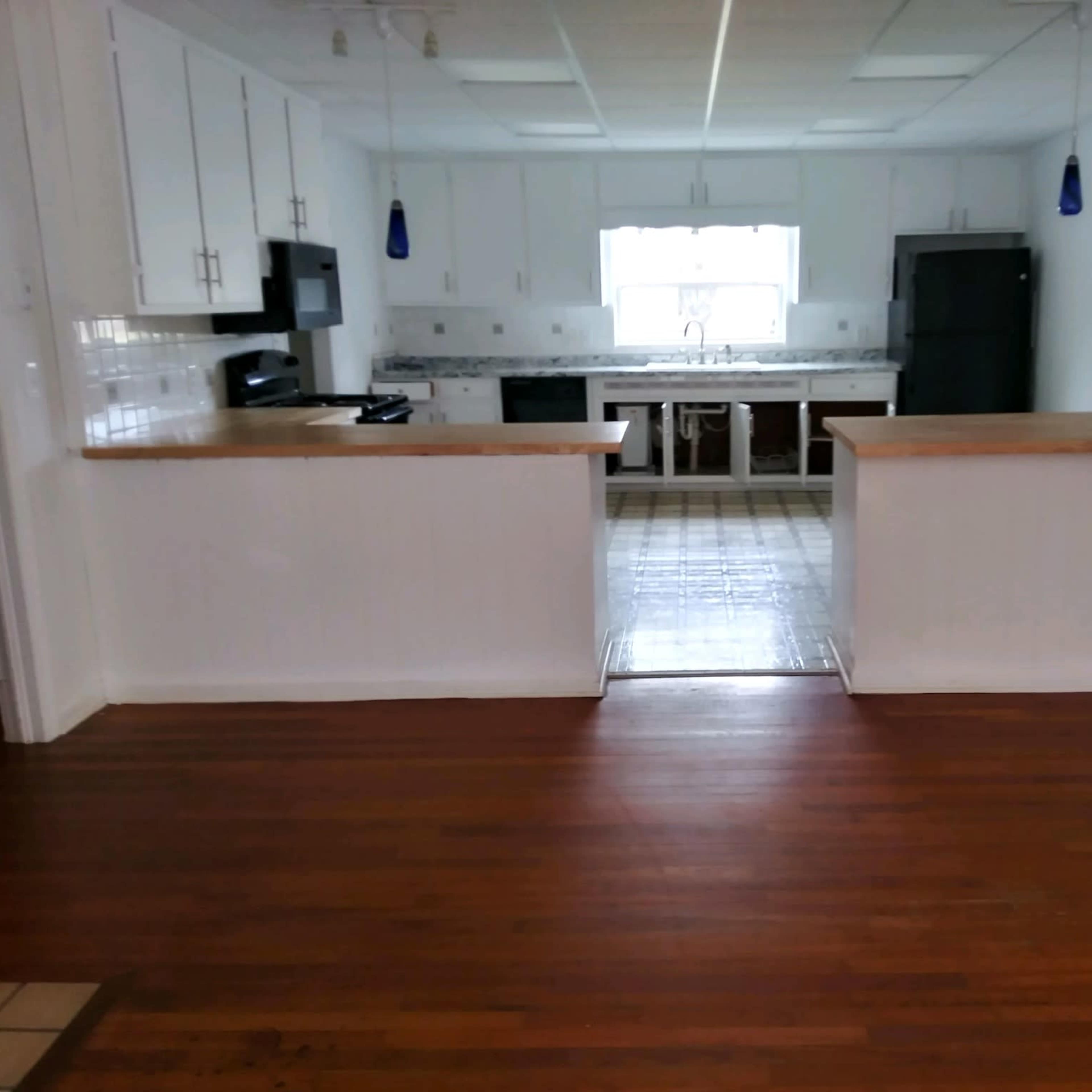 A kitchen with white cabinets, a central island, and wooden flooring, featuring a window providing natural light.