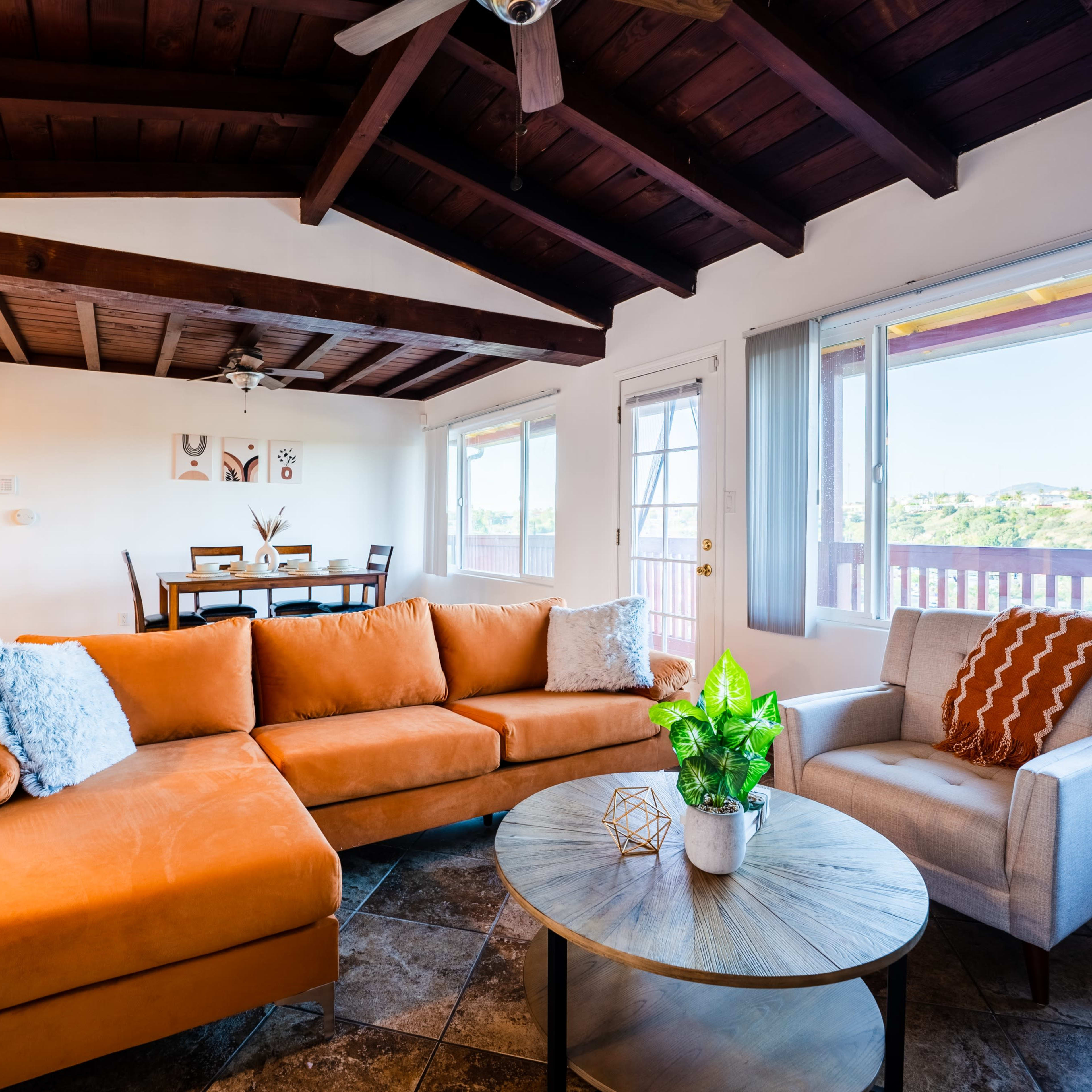 A cozy living room featuring an orange sectional sofa, a round coffee table, and large windows with views of the outdoors.